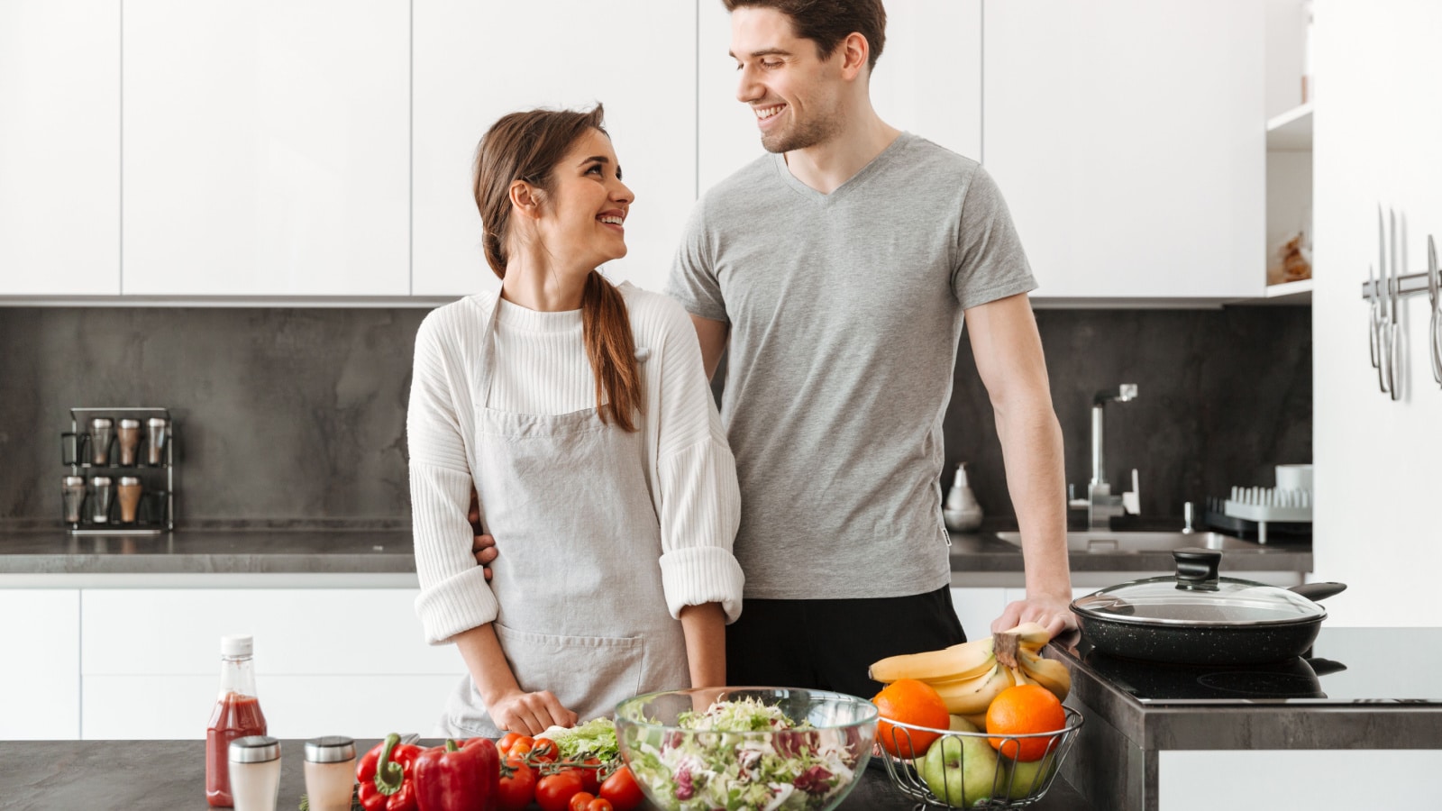 Portrait of a smiling young couple cooking together at the kitchen