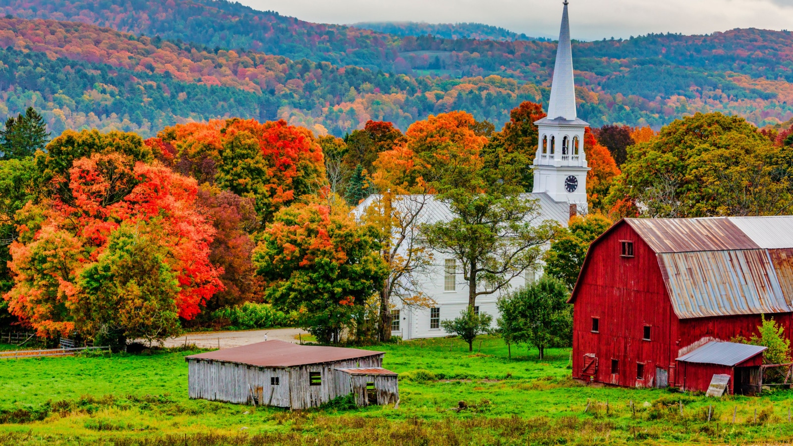 Woodstock, Vermont - October 8, 2018 - Red barn and church next to a harvested cornfiield with the Autumn colors in the background