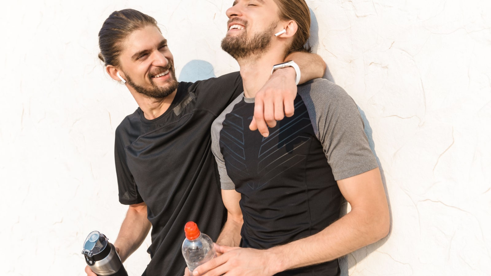 Two healthy fit twin brothers exercising outdoors, resting, drinking water over white wall background