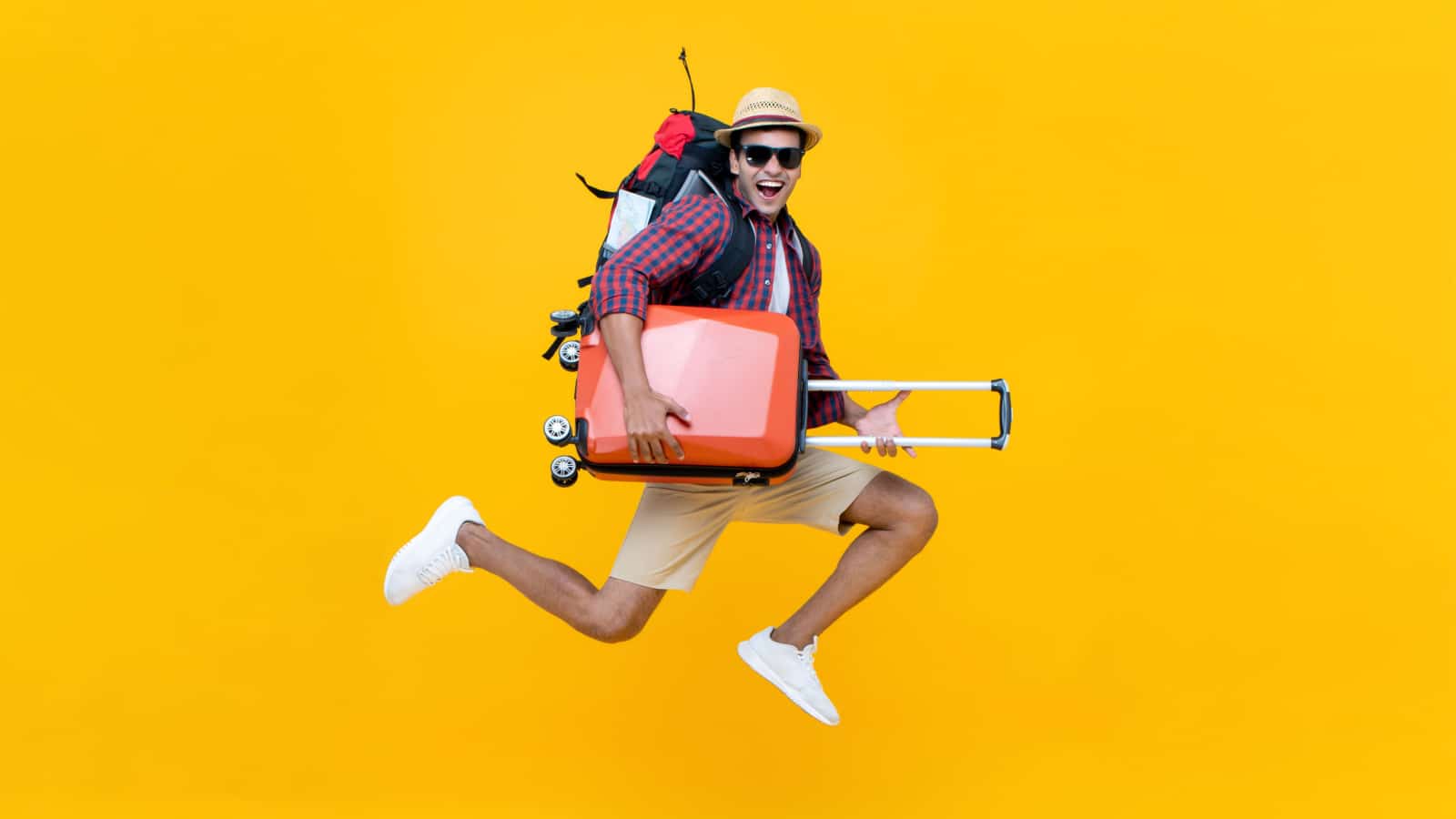 Excited happy young Asian man tourist with luggage jumping isolated on yellow studio background