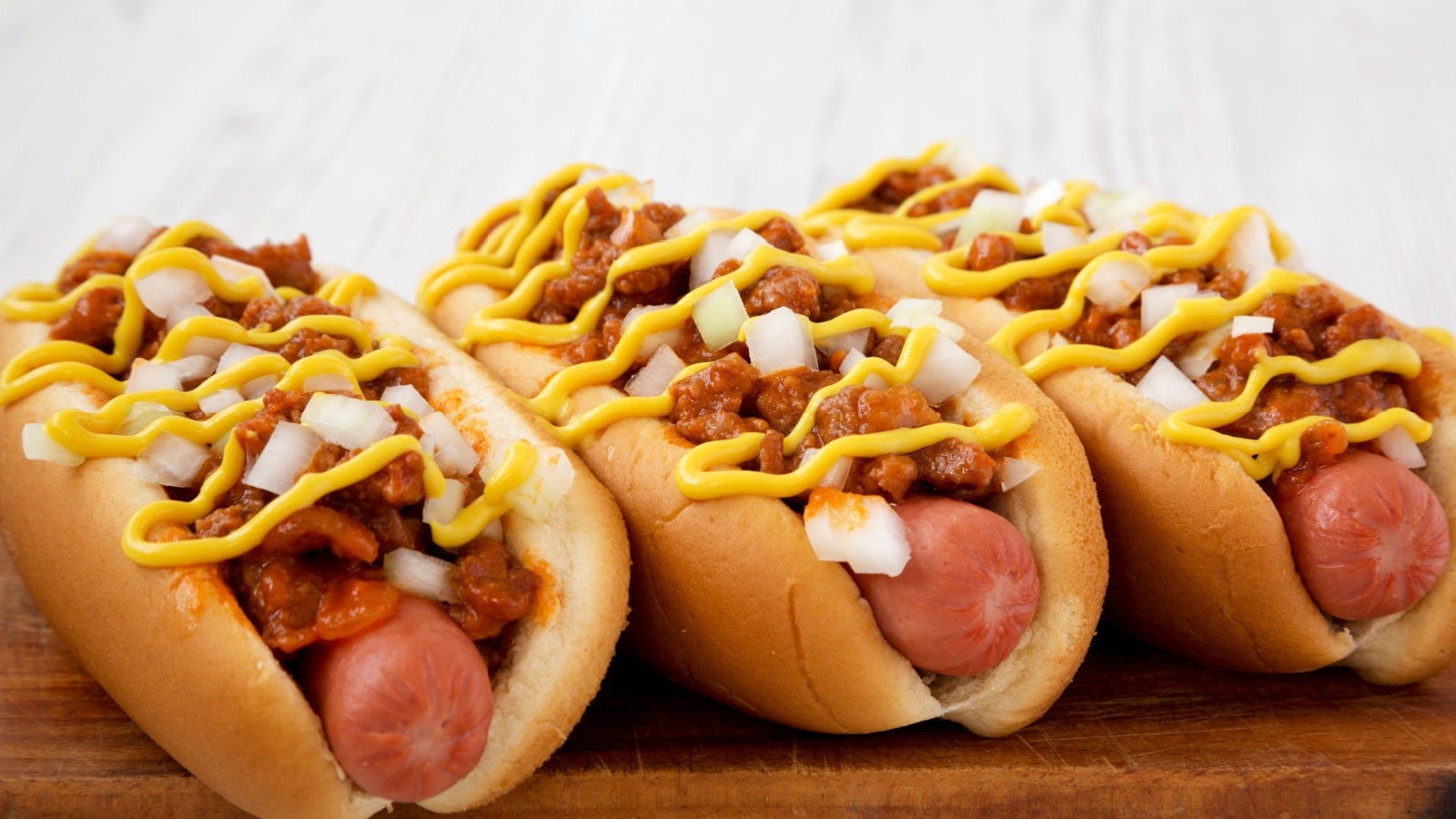 Homemade Coney Island hot dog on a rustic wooden board on a white wooden background, side view. Close-up.