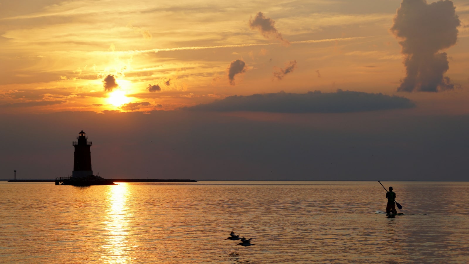 Silhouette of a light house, a kayak and birds flying above water during sunset at Cape Henlopen State Park, Lewes, Delaware, U.S.A