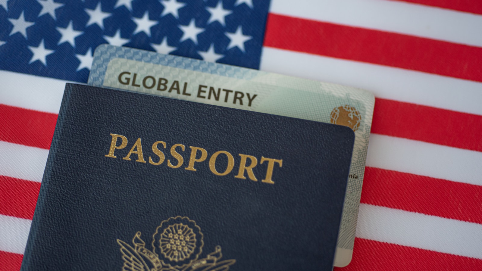 Global Entry card (Trusted traveller) covered of Passport of United states of America on American flag surface. Close up above view.