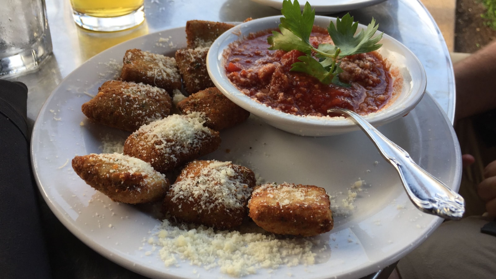 Toasted ravioli sprinkled with parmesan cheese with marinara sauce garnished with parsley on a white plate at an Italian restaurant on The Hill in St. Louis, Missouri, USA.
