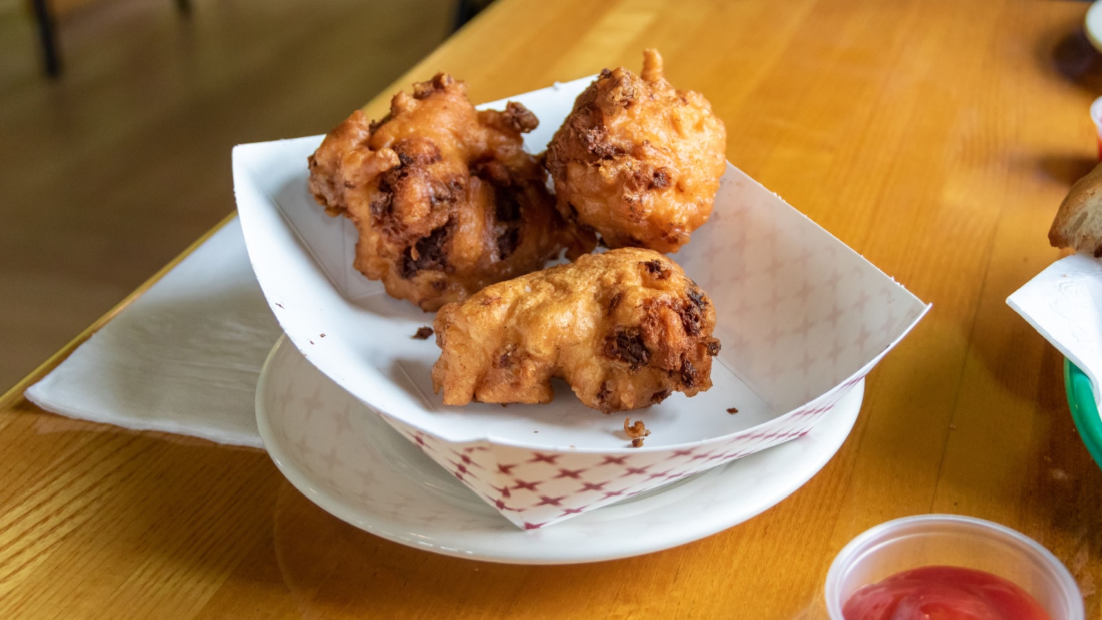 Fried Clam Cakes at a Rhode Island restaurant served in a paper basket on wooden table with condiments