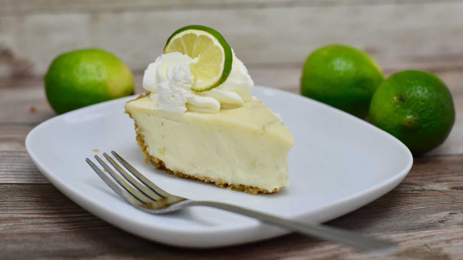 Slice of key lime pie on plate with limes