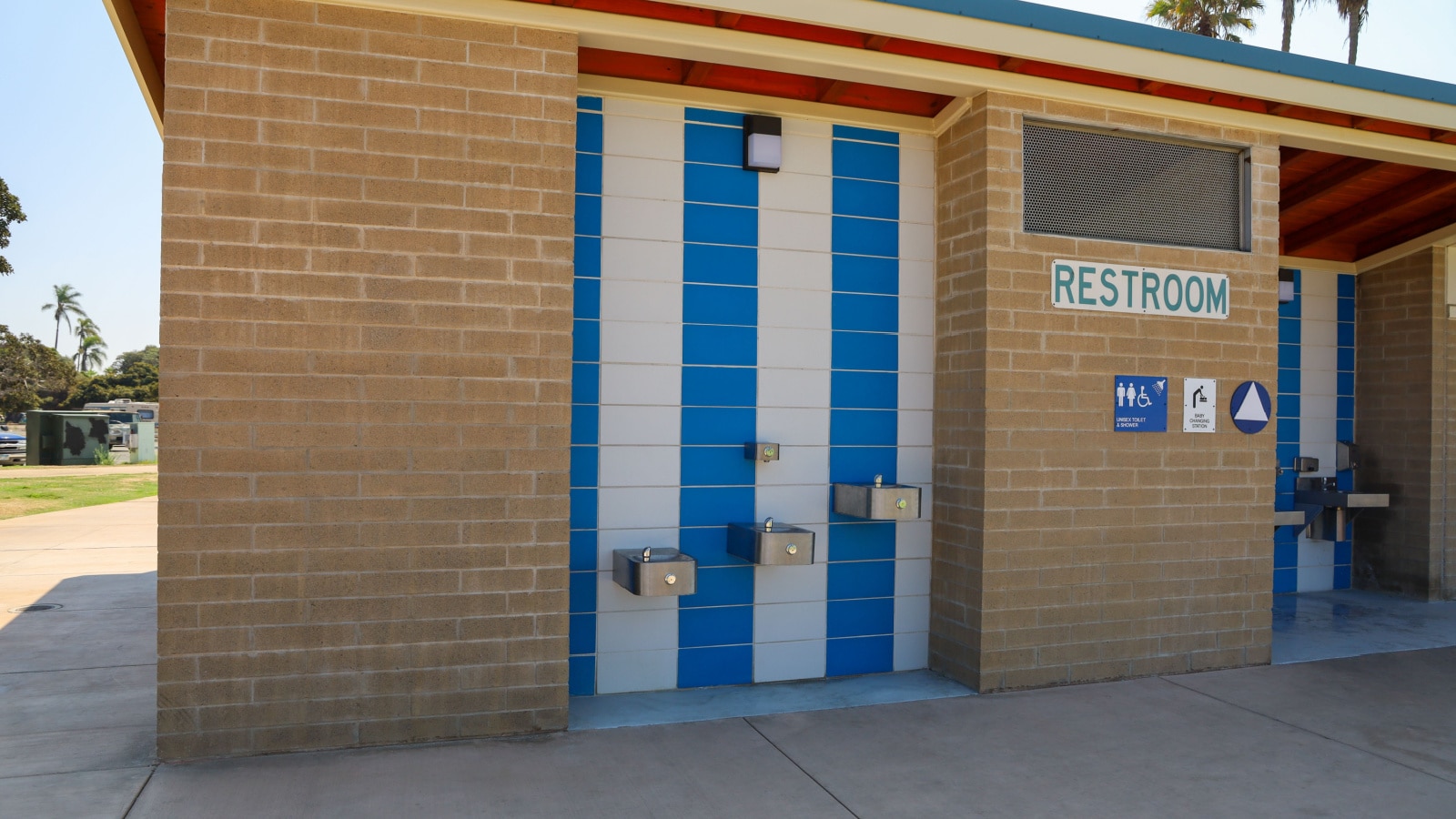 Beach park restroom entrance with unisex toilet and shower and baby changing station signs. Short, medium and tall water fountains at public park