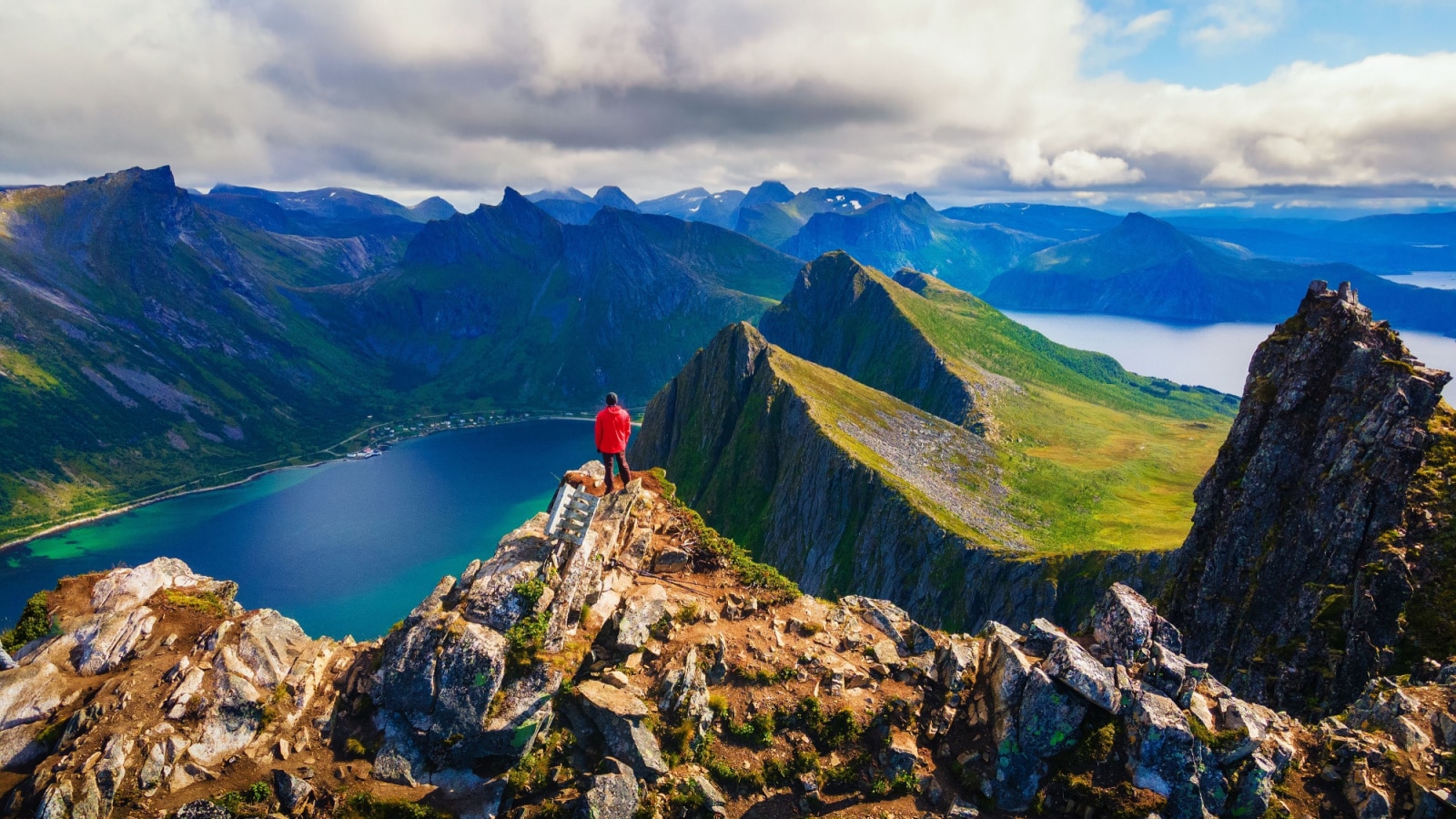 Hiker standing on the top of Husfjellet Mountain on Senja Island in northern Norway and enjoying spectacular views over surrounding fjords and mountains.