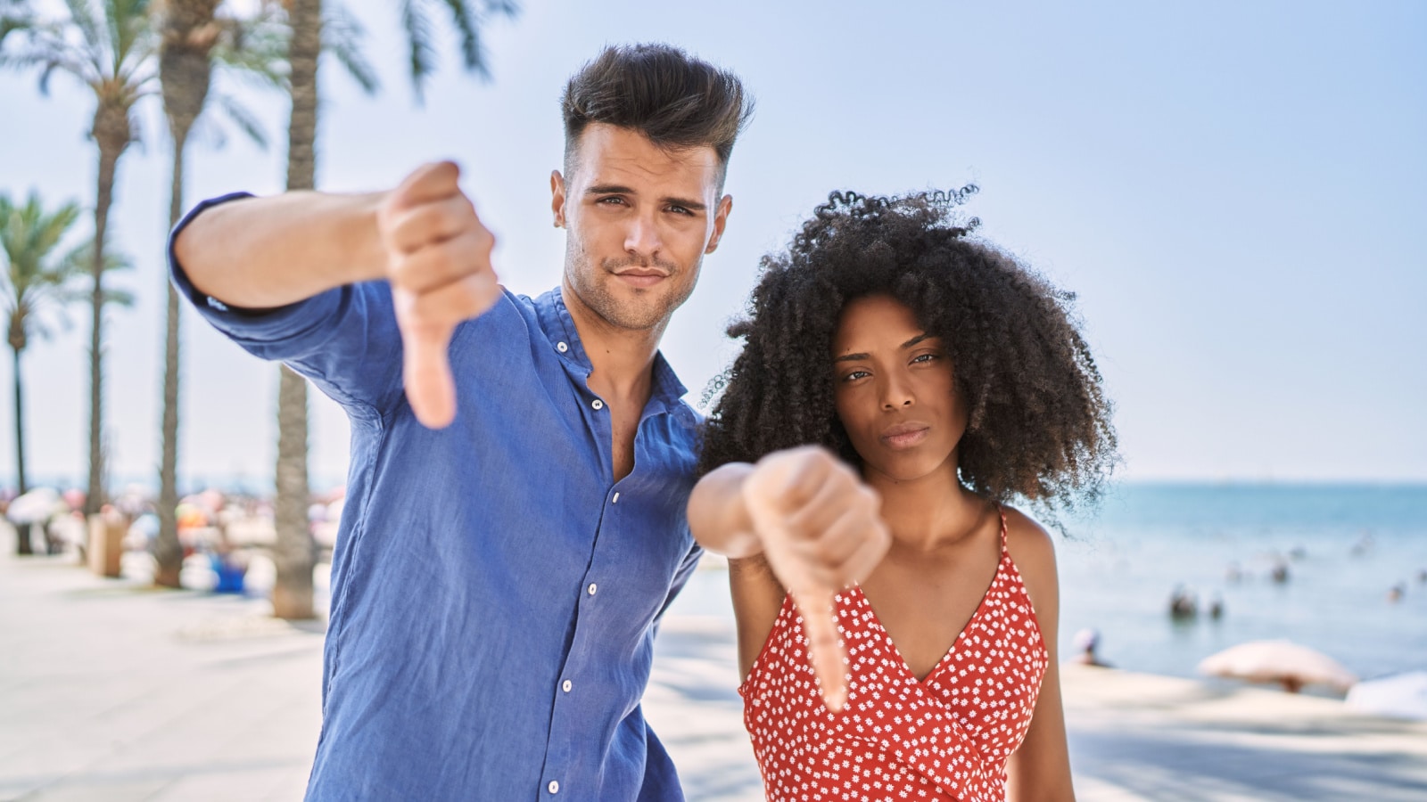 Young interracial couple outdoors on a sunny day looking unhappy and angry showing rejection and negative with thumbs down gesture. bad expression.