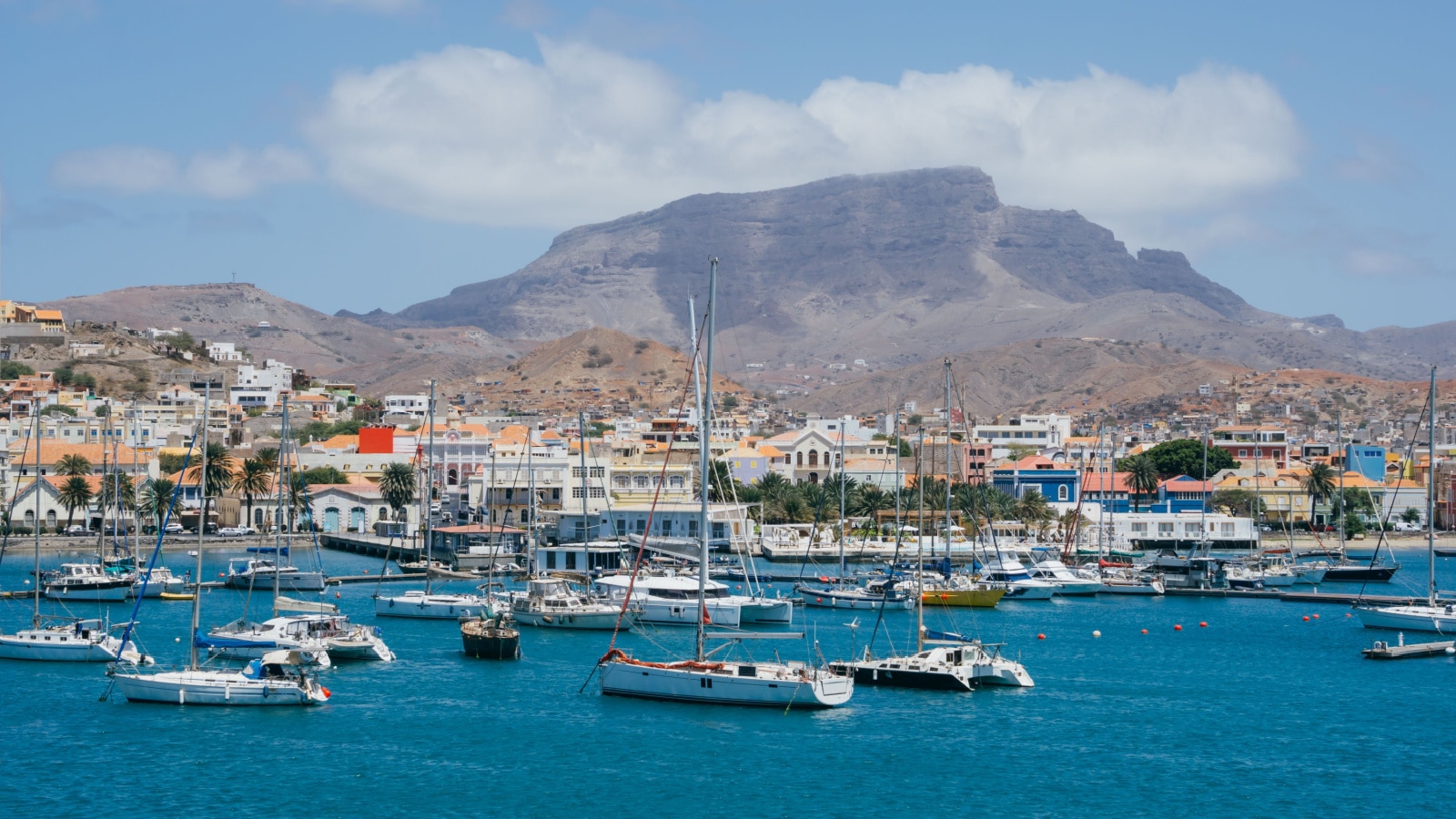 The sailboats in the bay against the background of Mindelo city and the brown mountain in a sunny day on Sao Vicente island in Cape Verde.