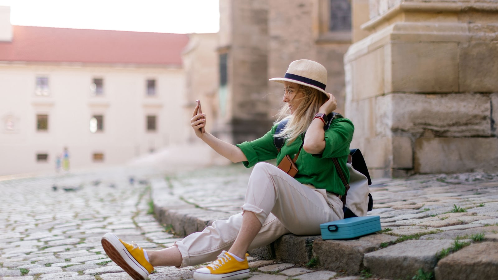 Young woman travel alone in old city centre, sitting and taking selfe.