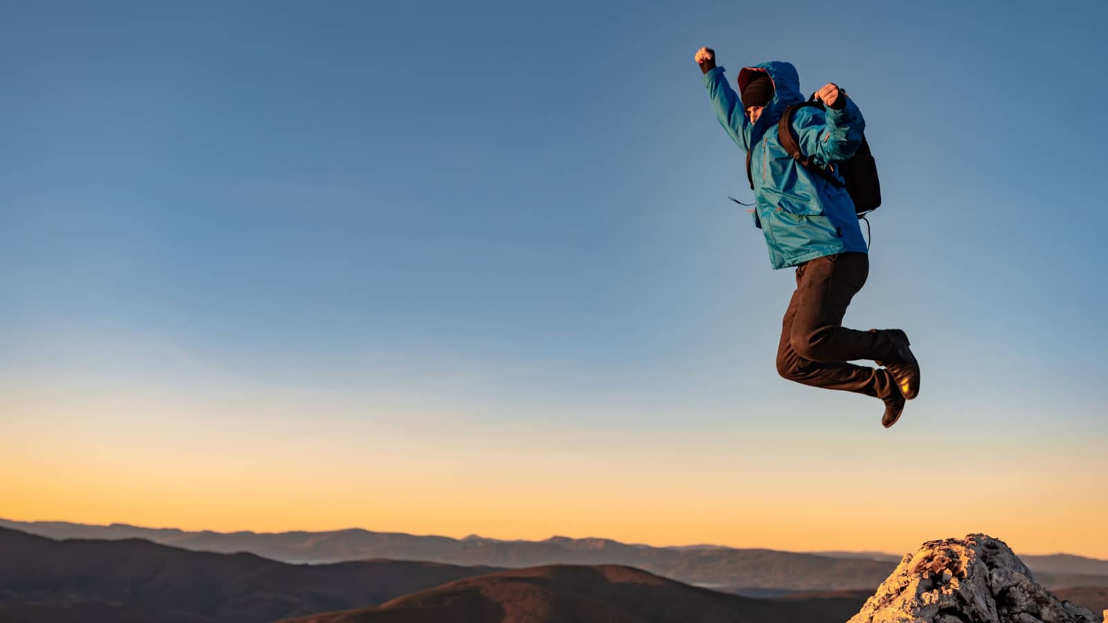 A happy joyful man jumping on top of a mountain concept of adventure travel extreme sport hiking.
