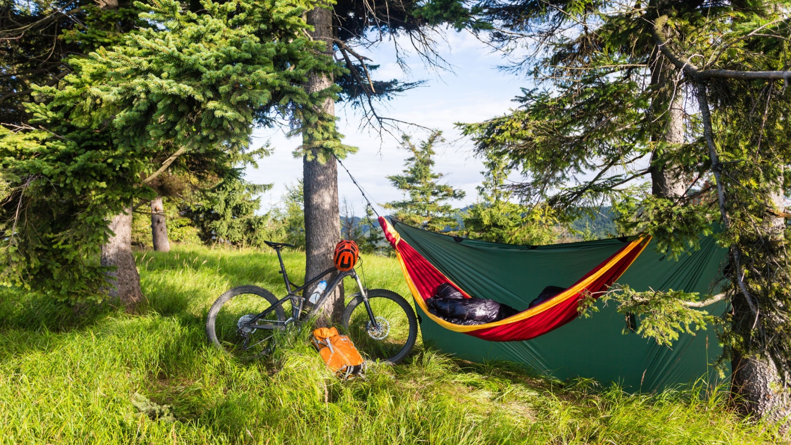 Camping in woods with hammock and sleeping bag on mountain biking adventure trip in green mountains. Travel campsite when mtb cycling with backpack. Lightweight shelter in wilderness forest, Poland.