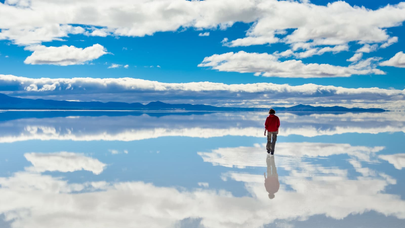 Girl in red on Salar de Uyuni in Bolivia covered with water with cloudy sky reflections