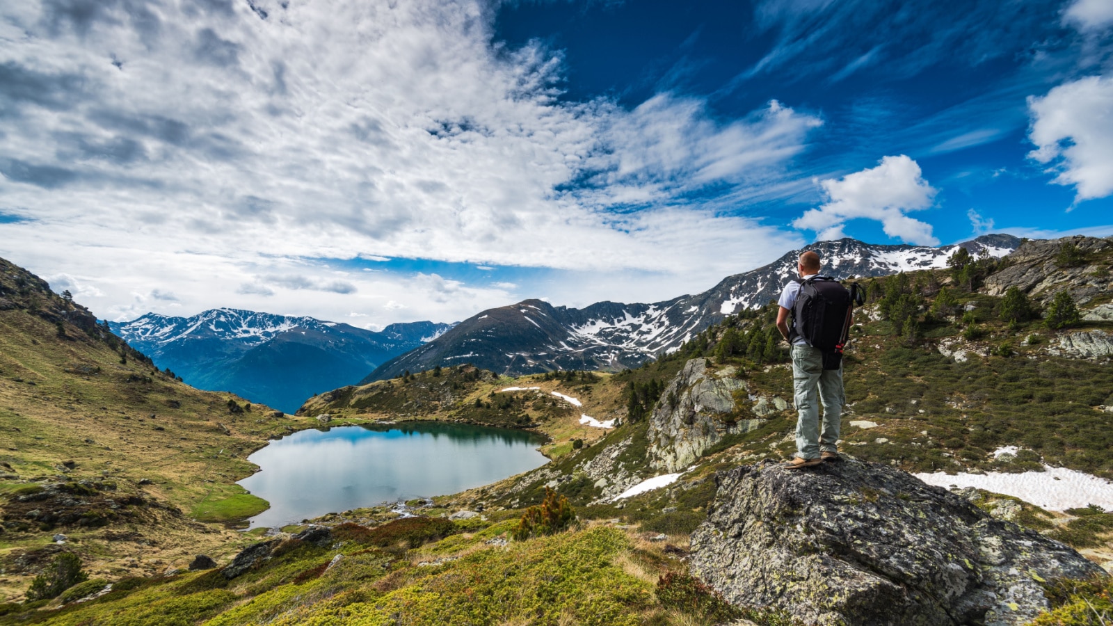 Active hiker with backpack in Pyrenees overlooking lake Tristaina in Andorra