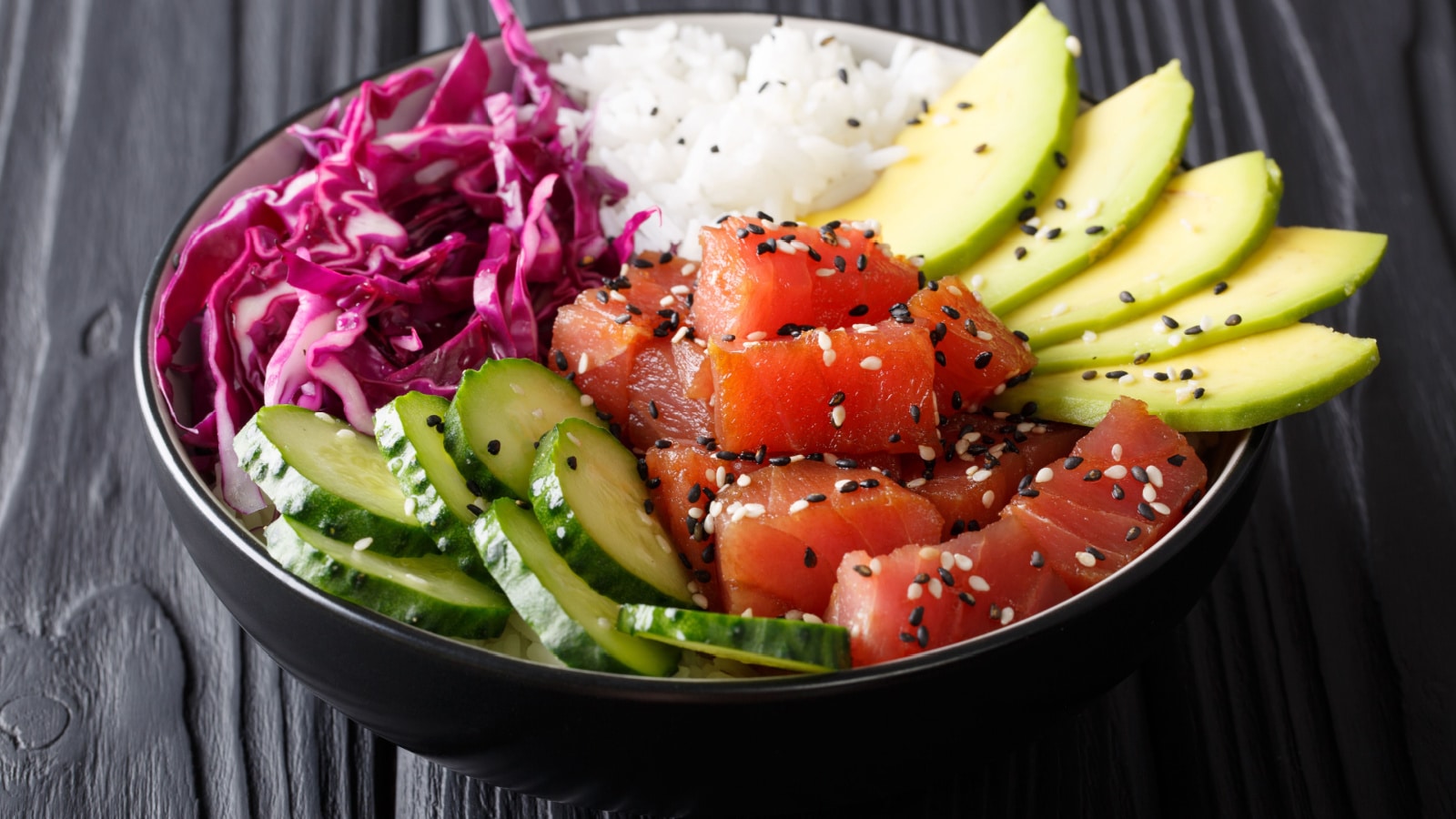 Organic food: tuna poke bowl with rice, fresh cucumbers, red cabbage and avocado close-up on the table. horizontal