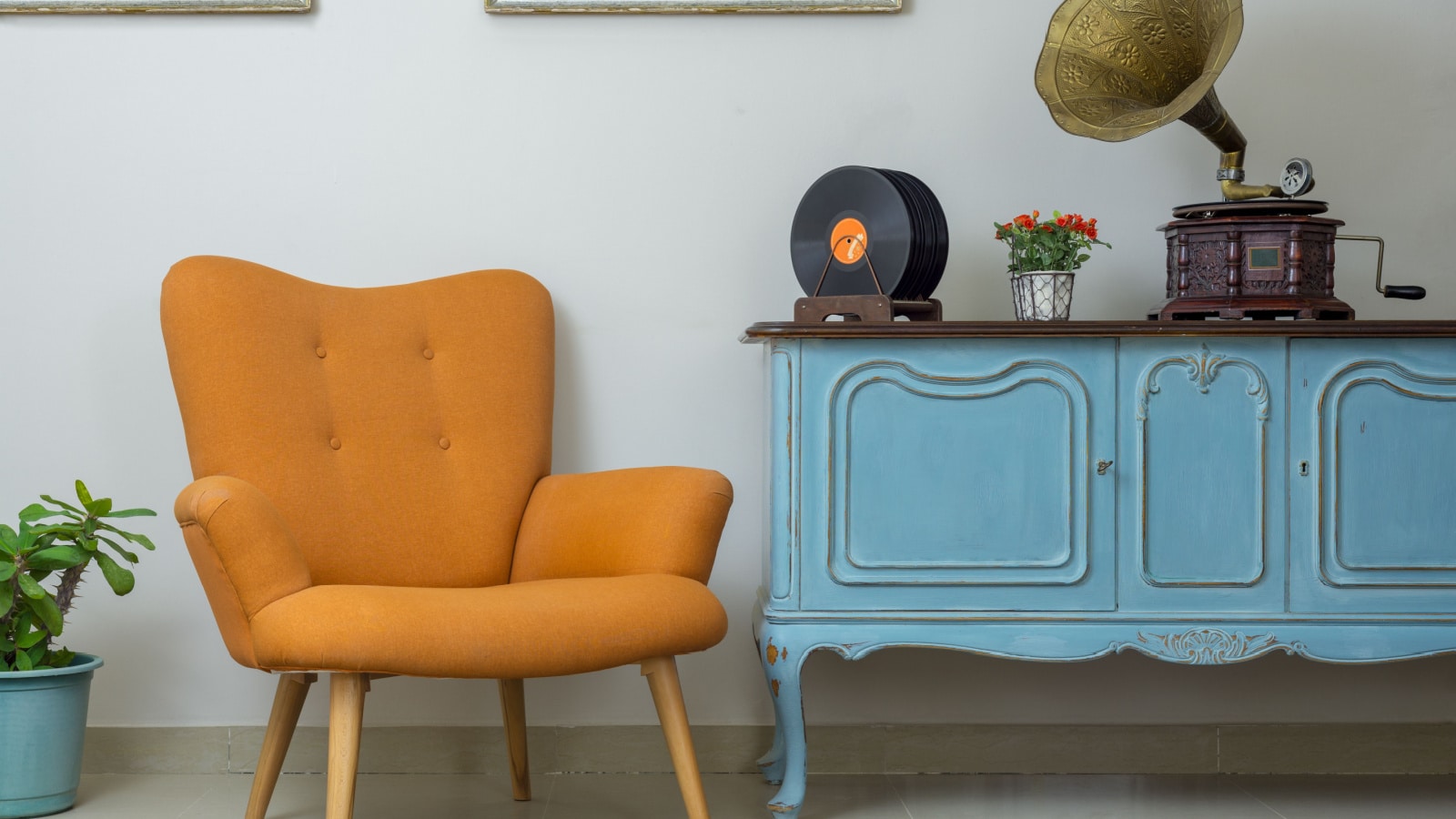 Vintage interior of retro orange armchair, vintage wooden light blue sideboard, old phonograph (gramophone), vinyl records on background of beige wall, tiled porcelain floor, and red carpet