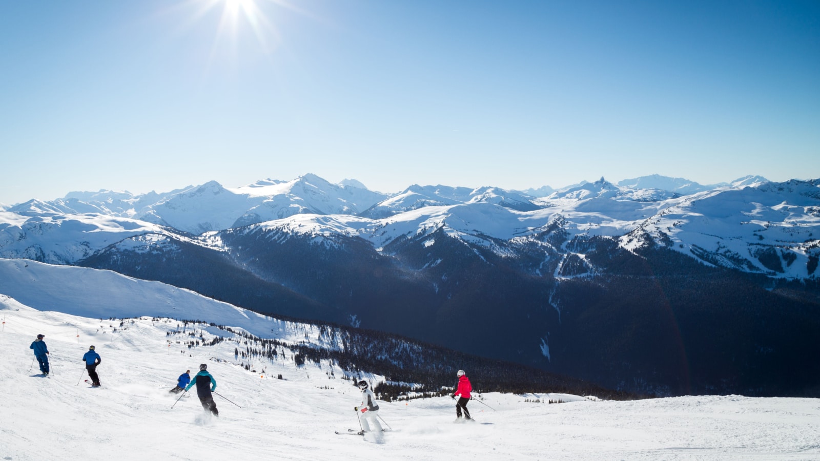 Skiers on a hill at the top of Blackcomb, 7th Heaven, with a view looking toward Whistler on a sunny day.