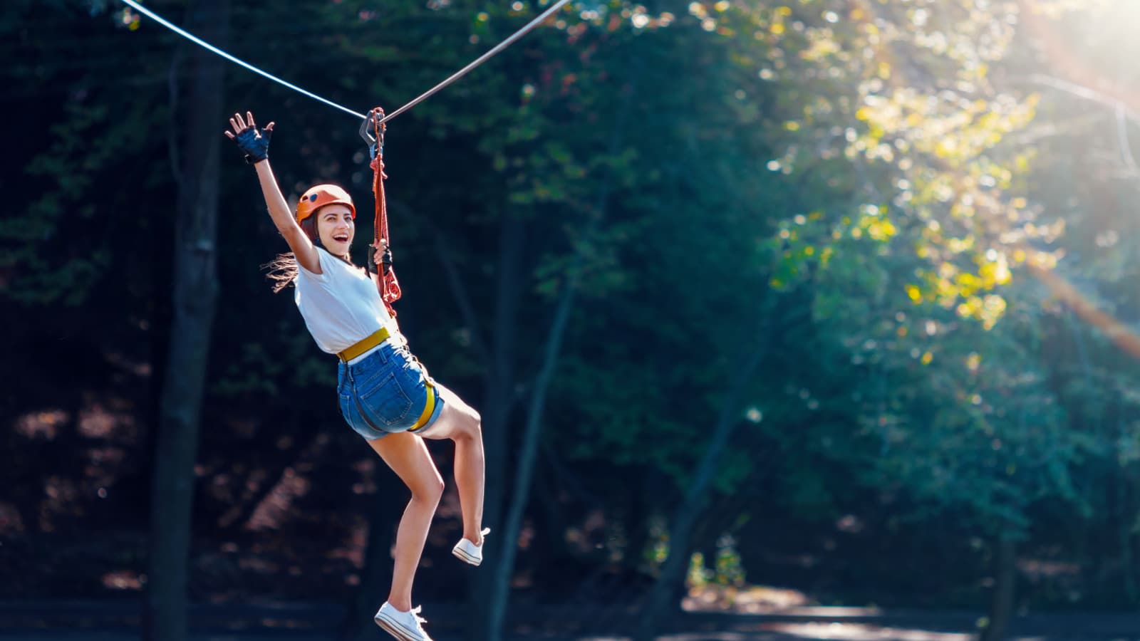 Happy women girl female gliding climbing in extreme road trolley zipline in forest on carabiner safety link on tree to tree top rope adventure park. Family weekend children kids activities concept