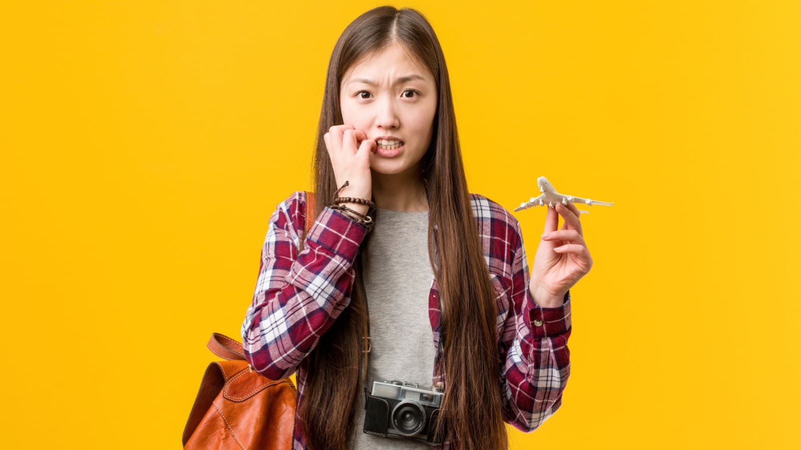 Young asian woman holding a airplane icon biting fingernails, nervous and very anxious.