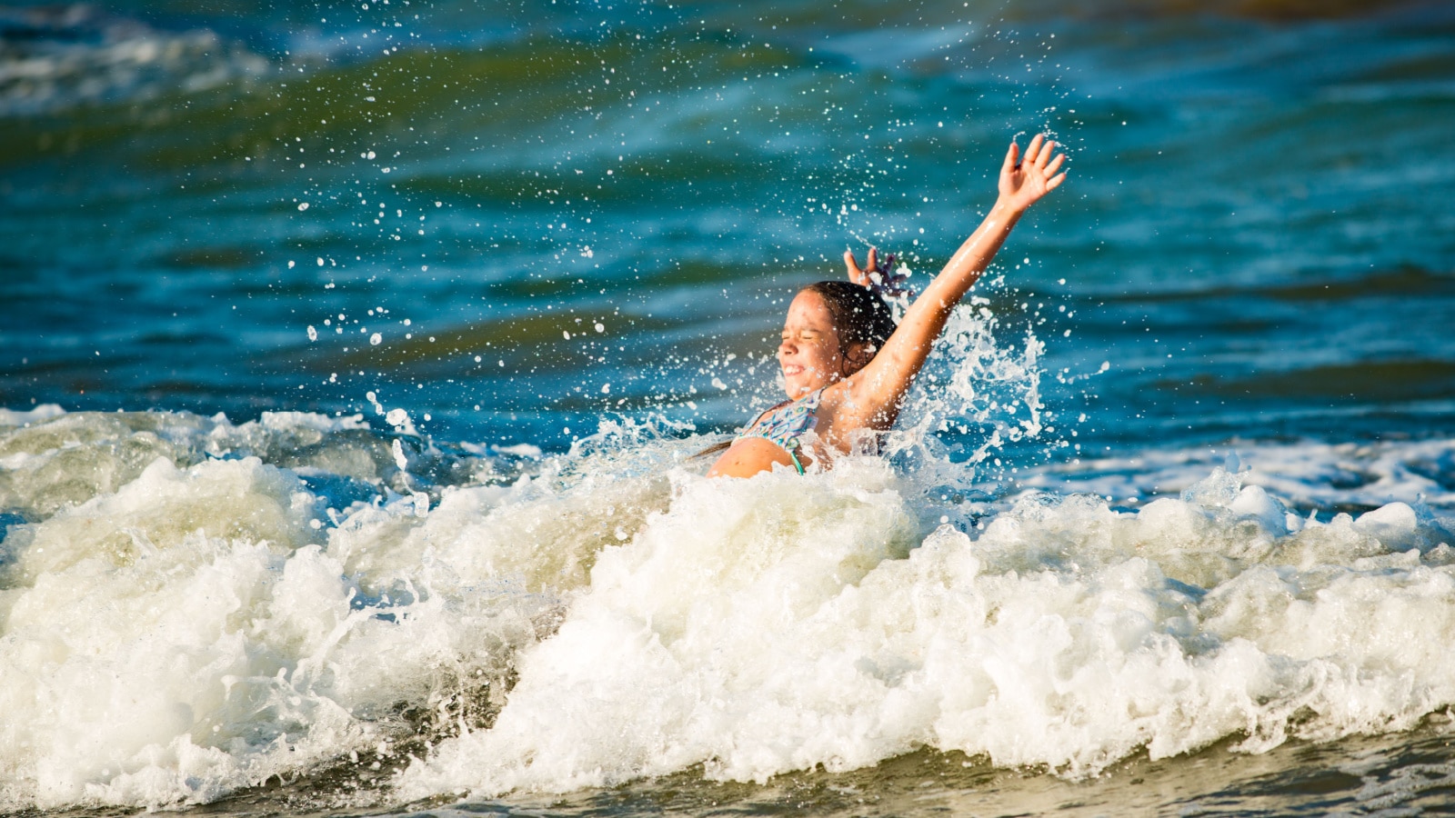 Emotional active little girl splashing in the stormy sea waves on a sunny summer day during the holidays. The concept of family holidays with children. Lovers of water and the elements