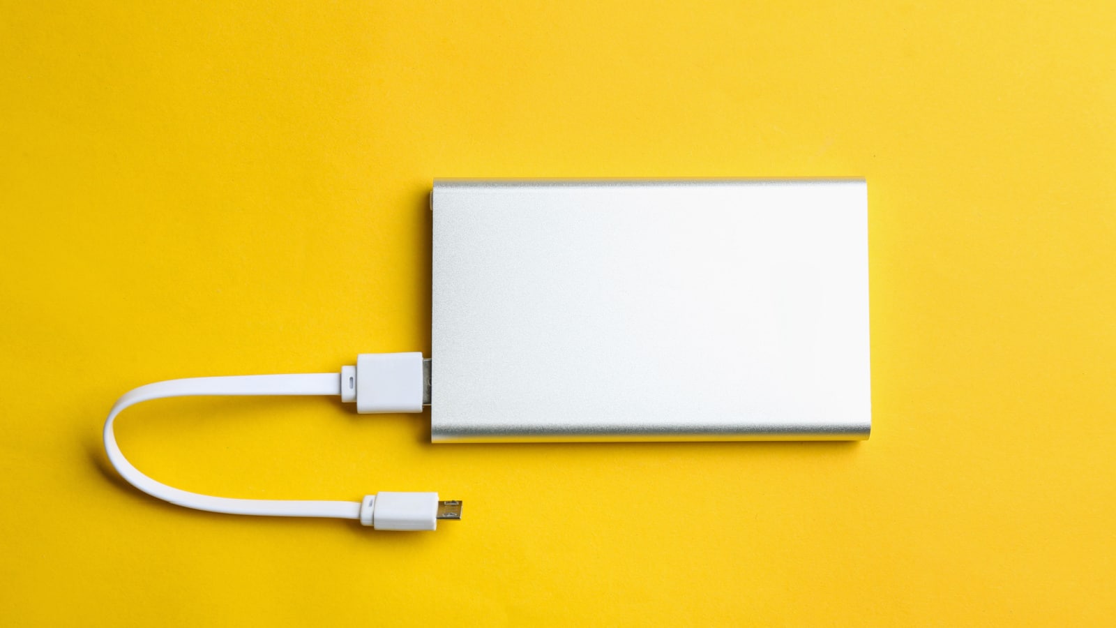 Modern portable charger with cable on yellow background, top view