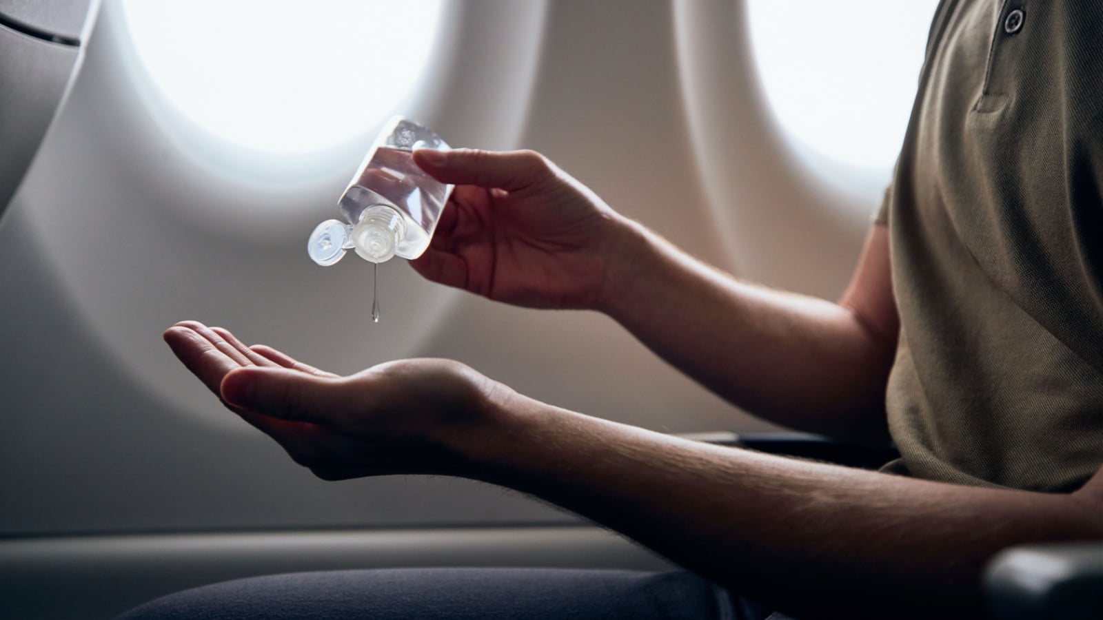 Man using hand sanitizer inside airplane during flight. Themes new normal, coronavirus and personal protection.