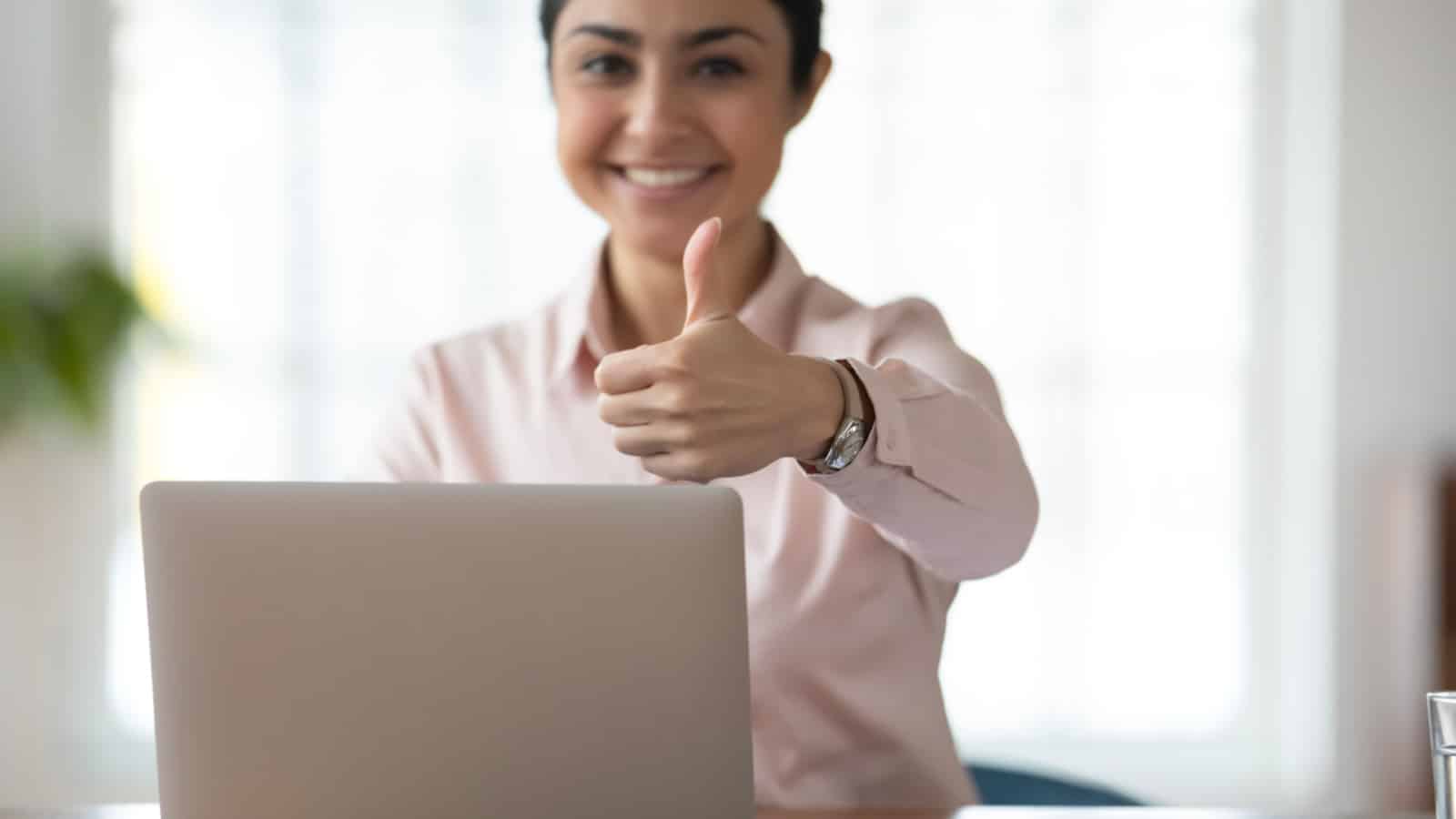 Close up portrait of smiling satisfied indian businesswoman show thumb up recommend online computer program. Happy ethnic female employee use laptop give recommendation to distant work or training.