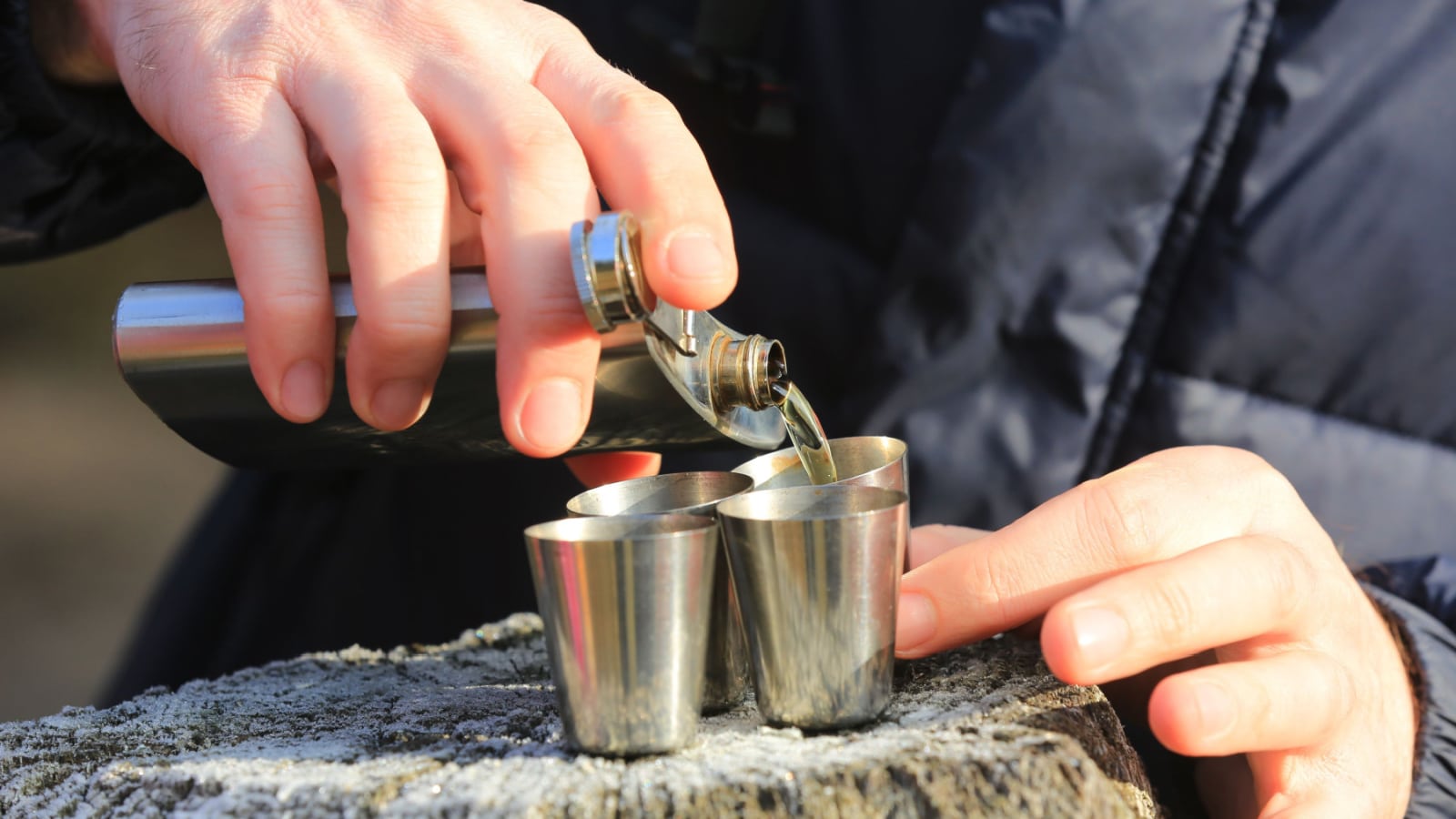 man pours alcohol from a flask into four steel glasses