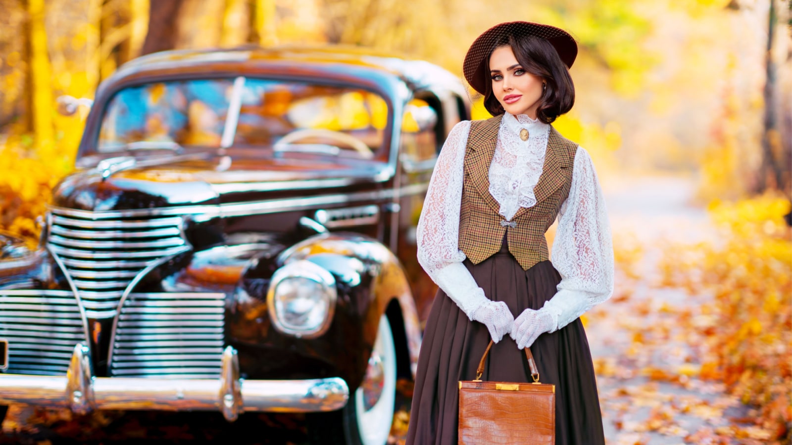 Beautiful female in vintage dress, lace blouse and hat with veil standing near retro brown car on autumn background. Elegant lady in gloves posing on nature.Warm art work.