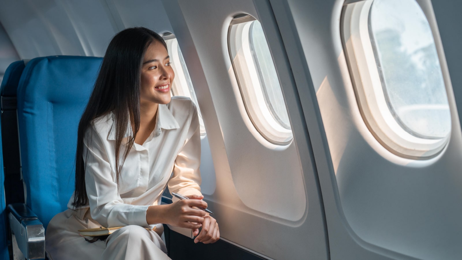 Asian woman sitting in a seat in airplane and looking out the window going on a trip vacation travel concept