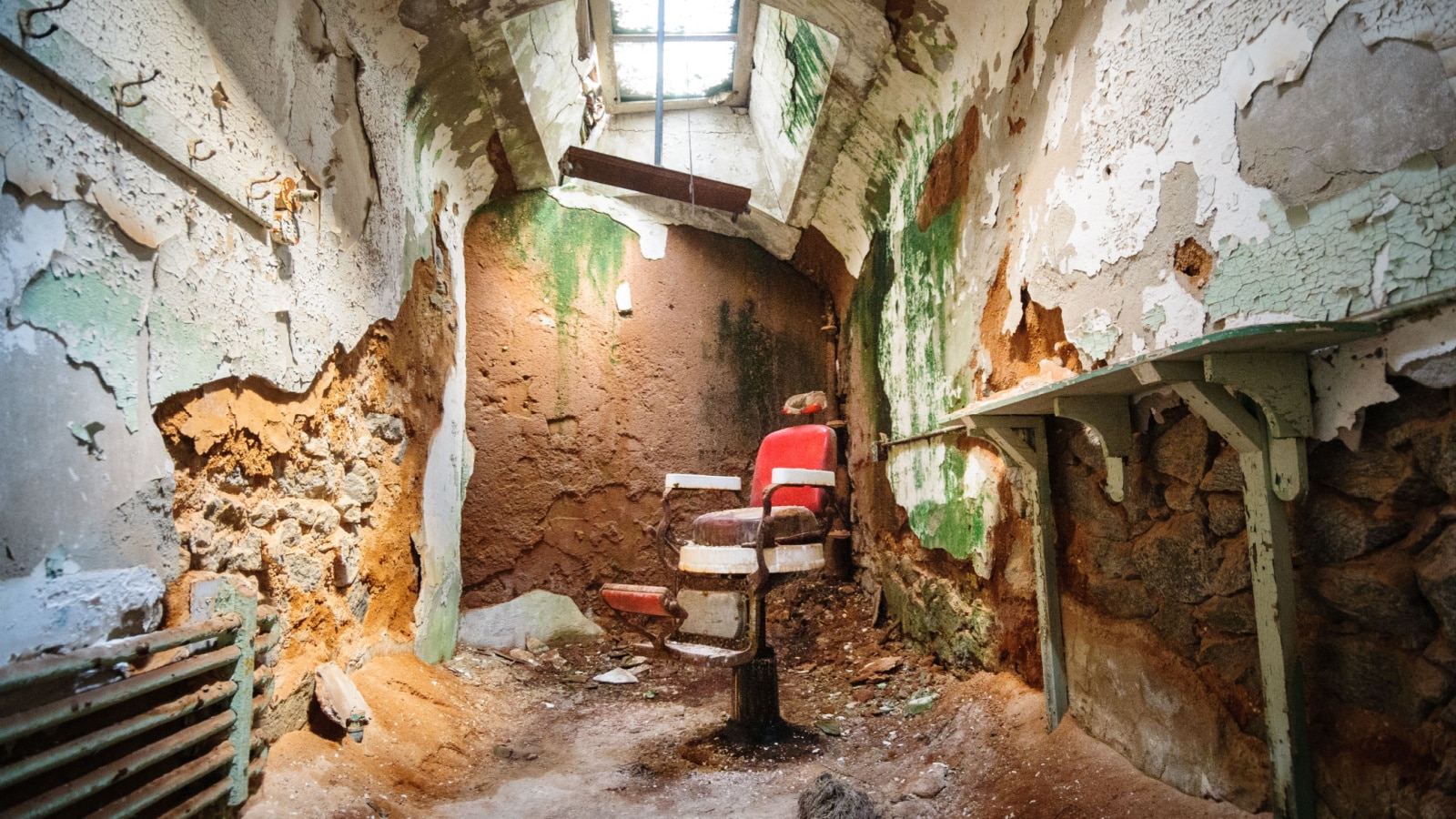 A dilapidated room inside the abandoned Eastern State Penitentiary in Philadelphia. Crumbling stone walls surround an old, rusted doctors chair in the center of the room.