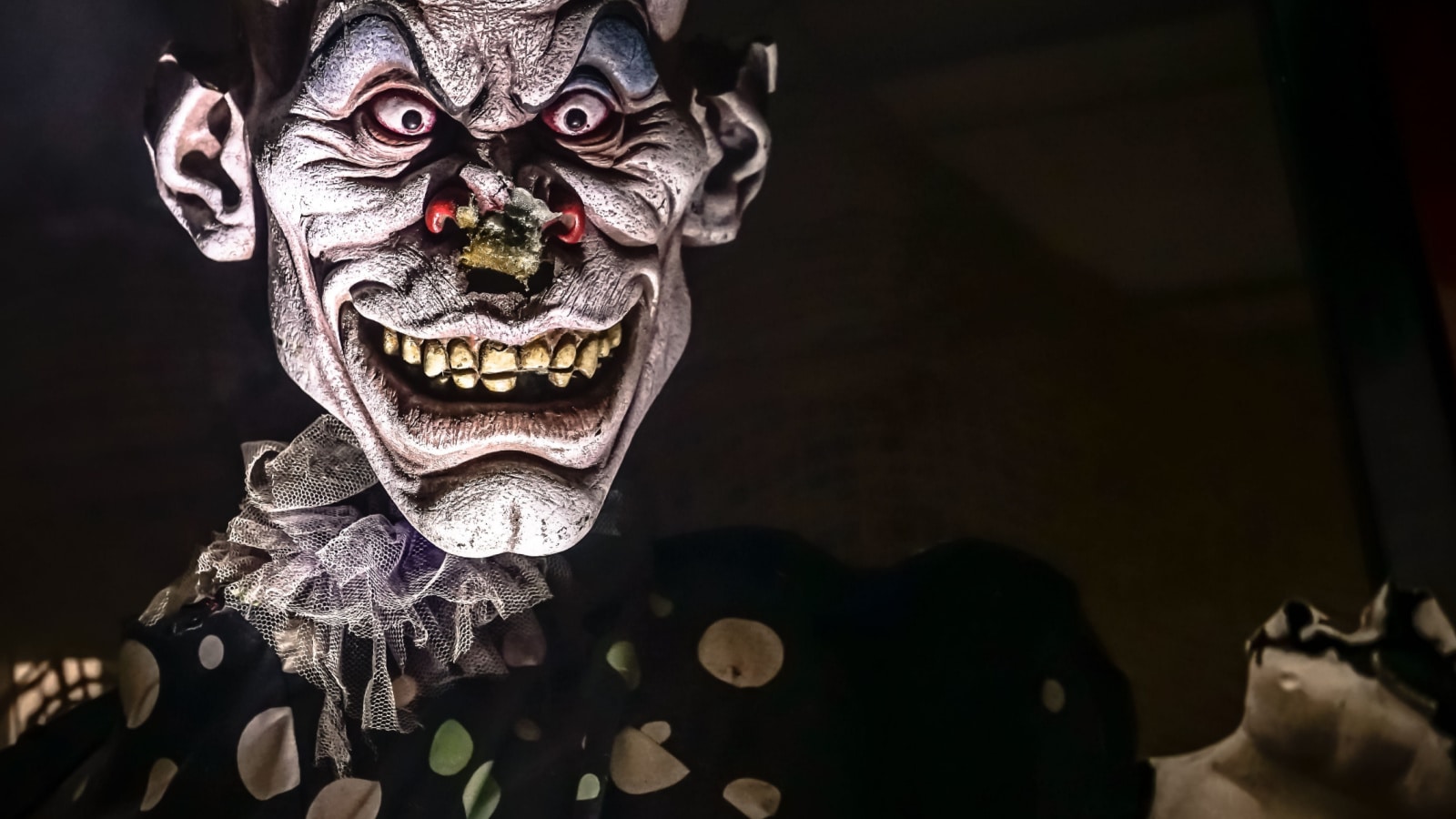 A frightening, disfigured, wrinkled wax clown figure startling passersby at the amusement theme park.