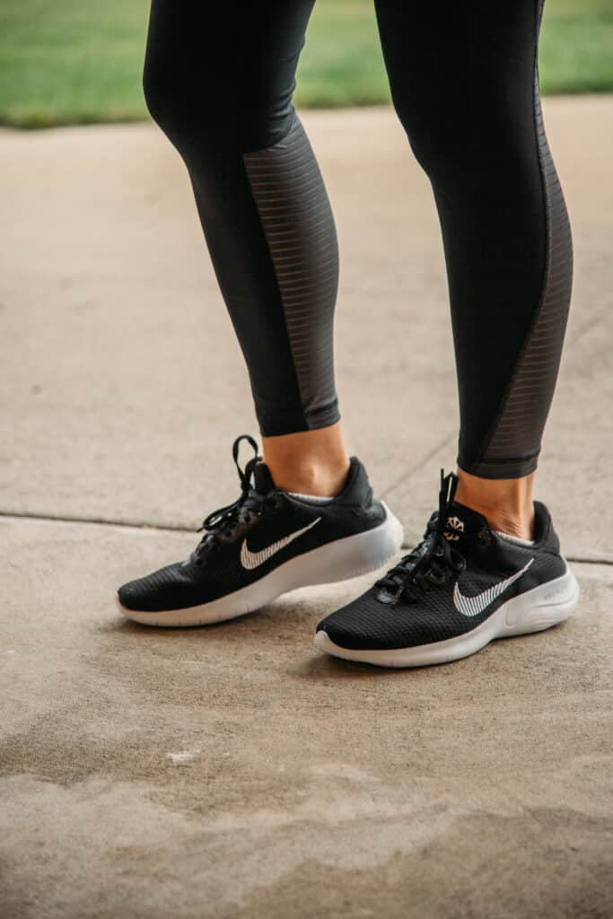 Lindsey wearing Nike running shoes that are black with white Nike logos and black running leggings standing on concrete