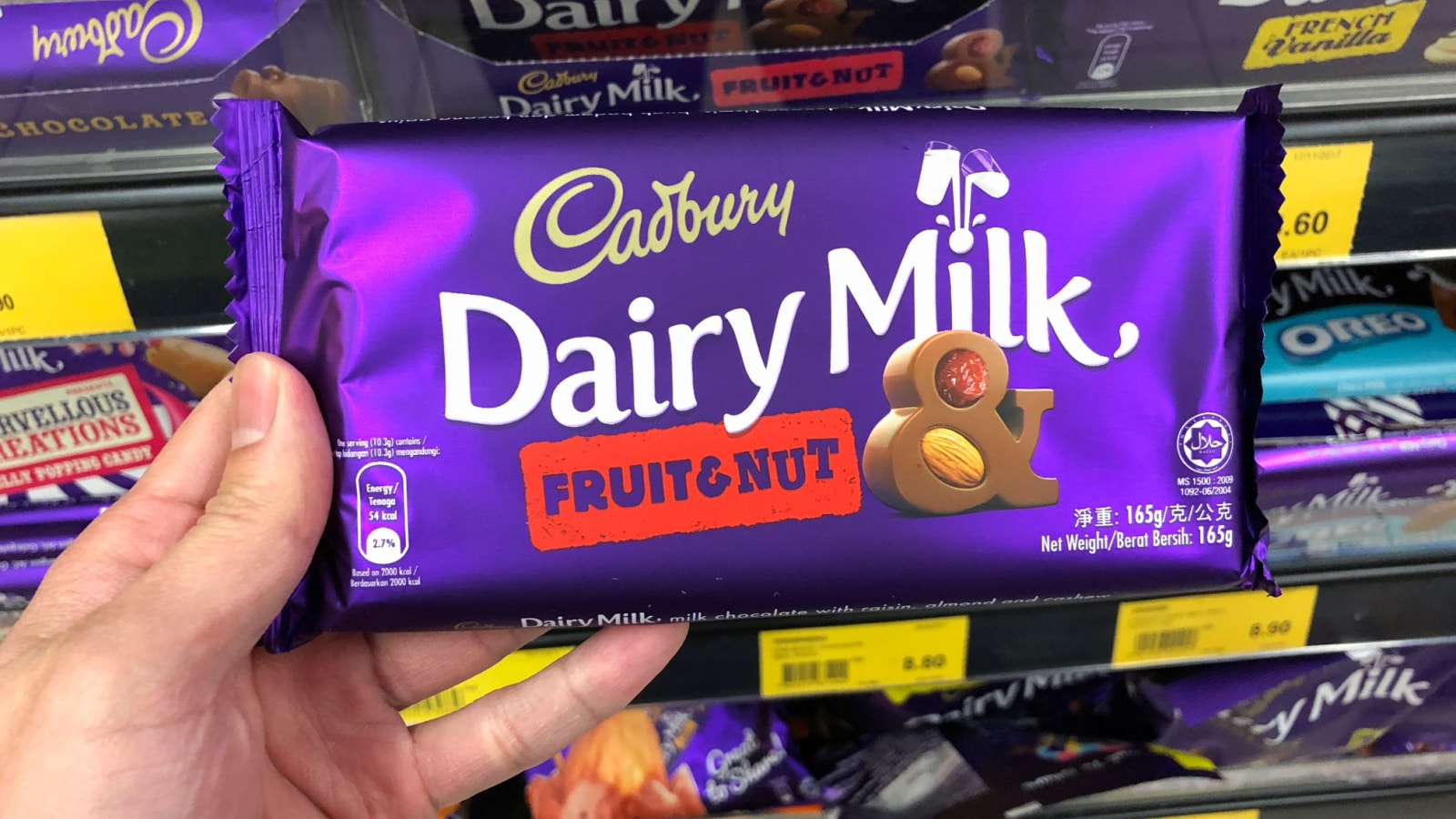 SHAH ALAM, MALAYSIA - FEBRUARY 12, 2018: Hand holding Cadbury Dairy Milk chocolate bar display on supermarket shelf for sale. Cadbury. Dairy Milk is a brand of milk chocolate manufactured by Cadbury.