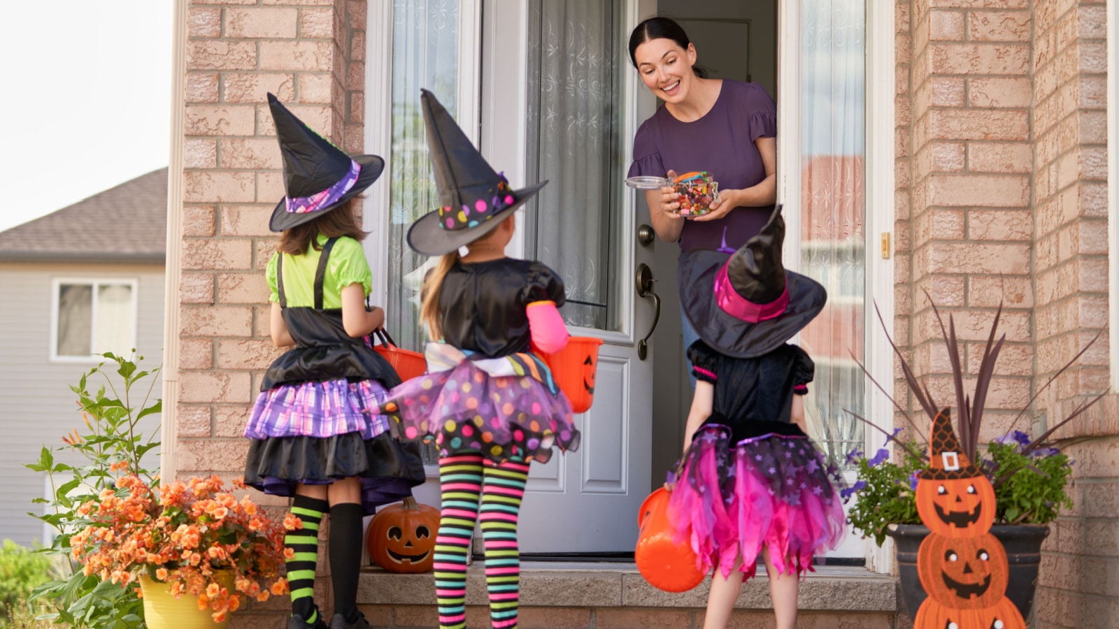 Happy family celebrating Halloween! Young mom treats children with candy. Funny kids in carnival costumes.