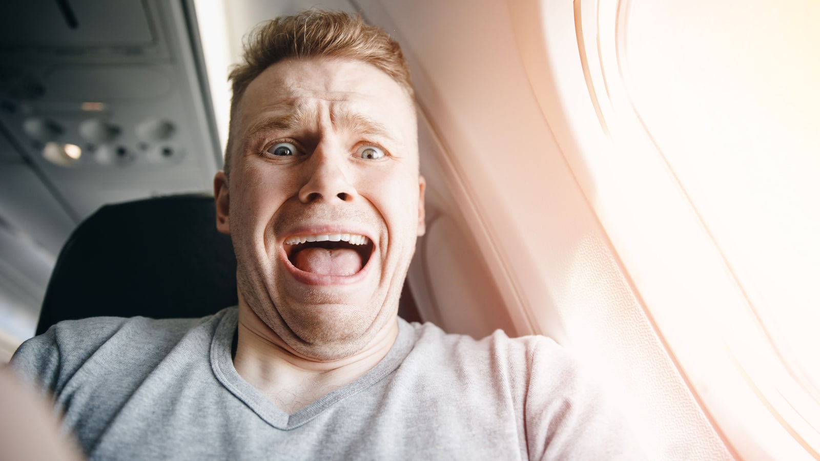 Male passenger in plane screams and cries, aerophobia. background of porthole. Concept fear of flying on airplane.