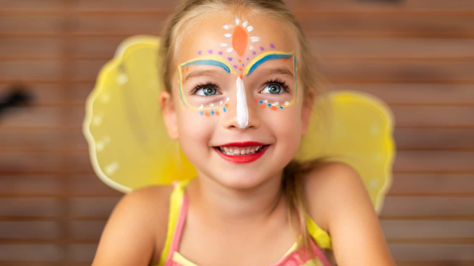 Waist up portrait of cute preschooler with DIY face paint wearing a butterfly halloween or carnival costume.