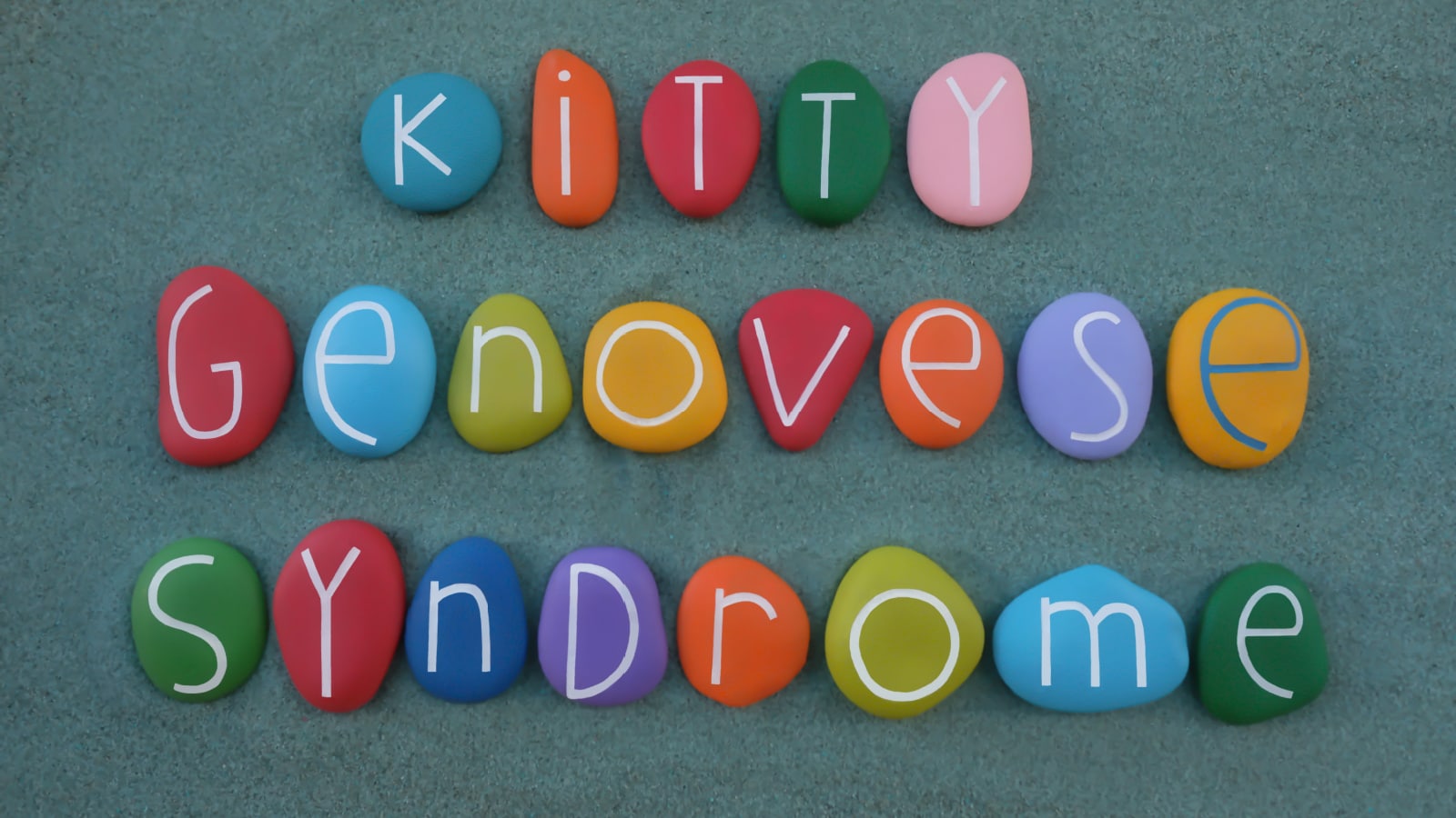 Kitty Genovese Syndrome text composed with multi colored stone letters on green sand