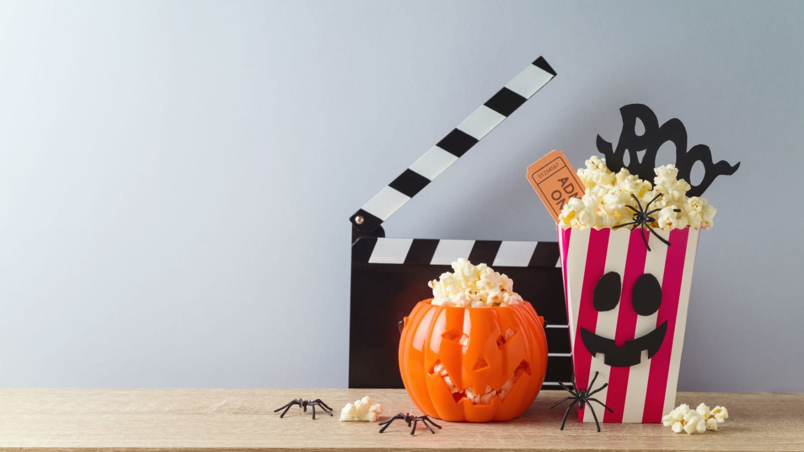 Horror movie night and Halloween party concept with jack o lantern pumpkin, popcorn and movie clapperboard on wooden table