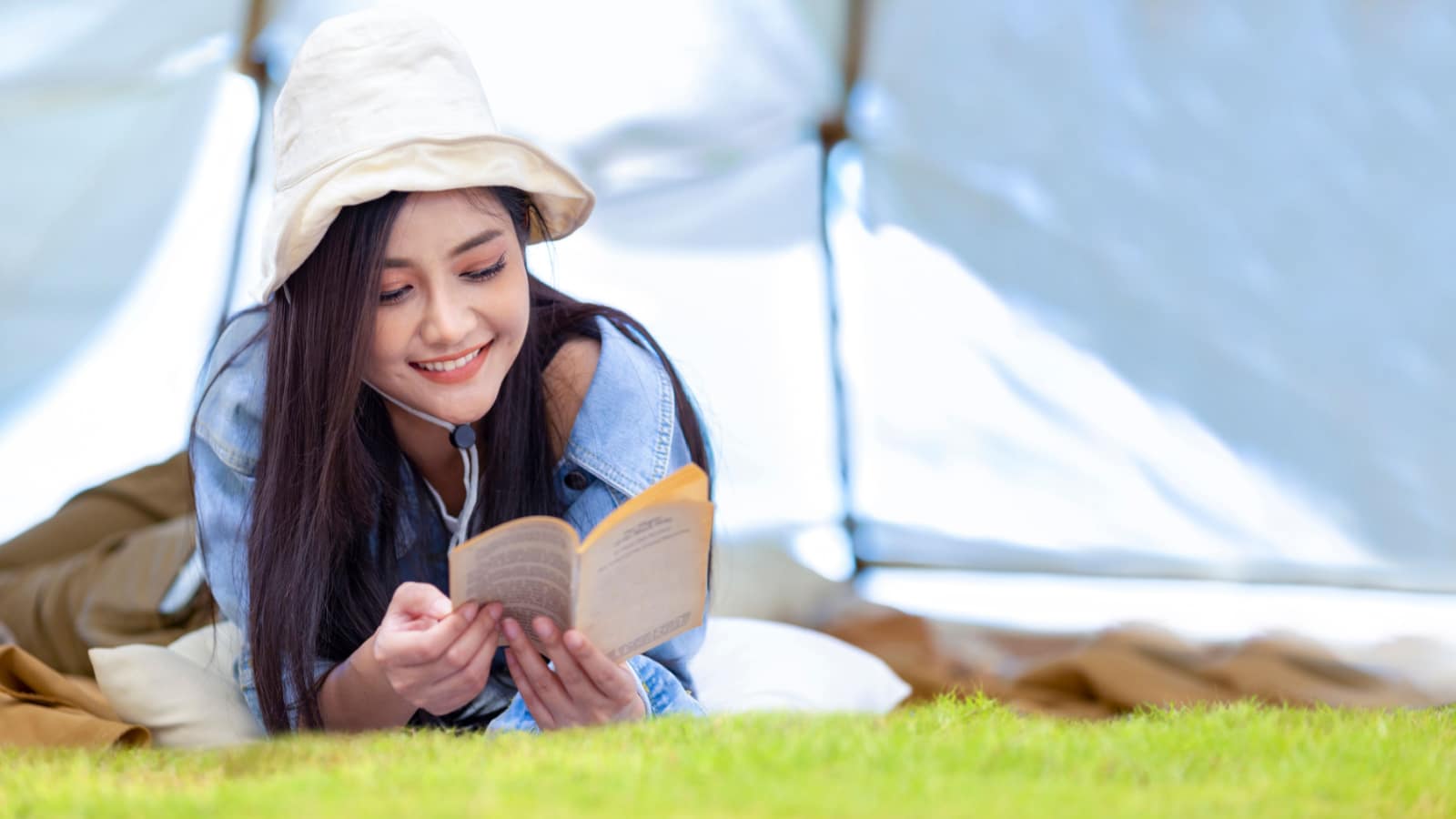 Asian woman is reading a book in her tent while camping outdoor during summer time in national park for adventure and active travel getaway, digital detox concept