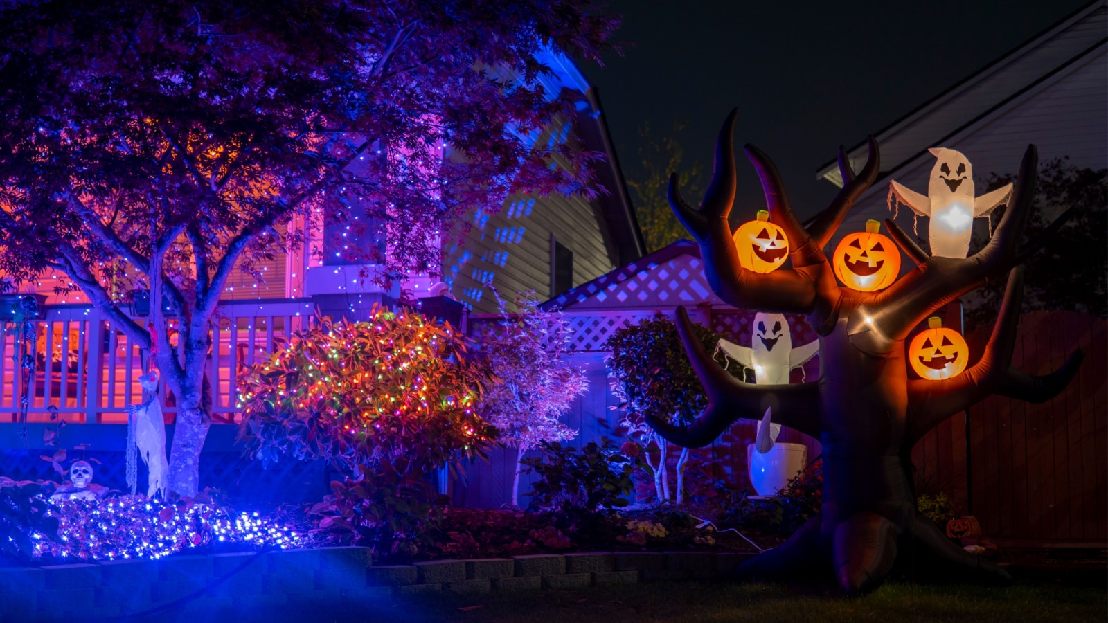 Night Halloween house outdoor decorations with glowing inflatable pumpkins and ghosts purple lights and orange garlands