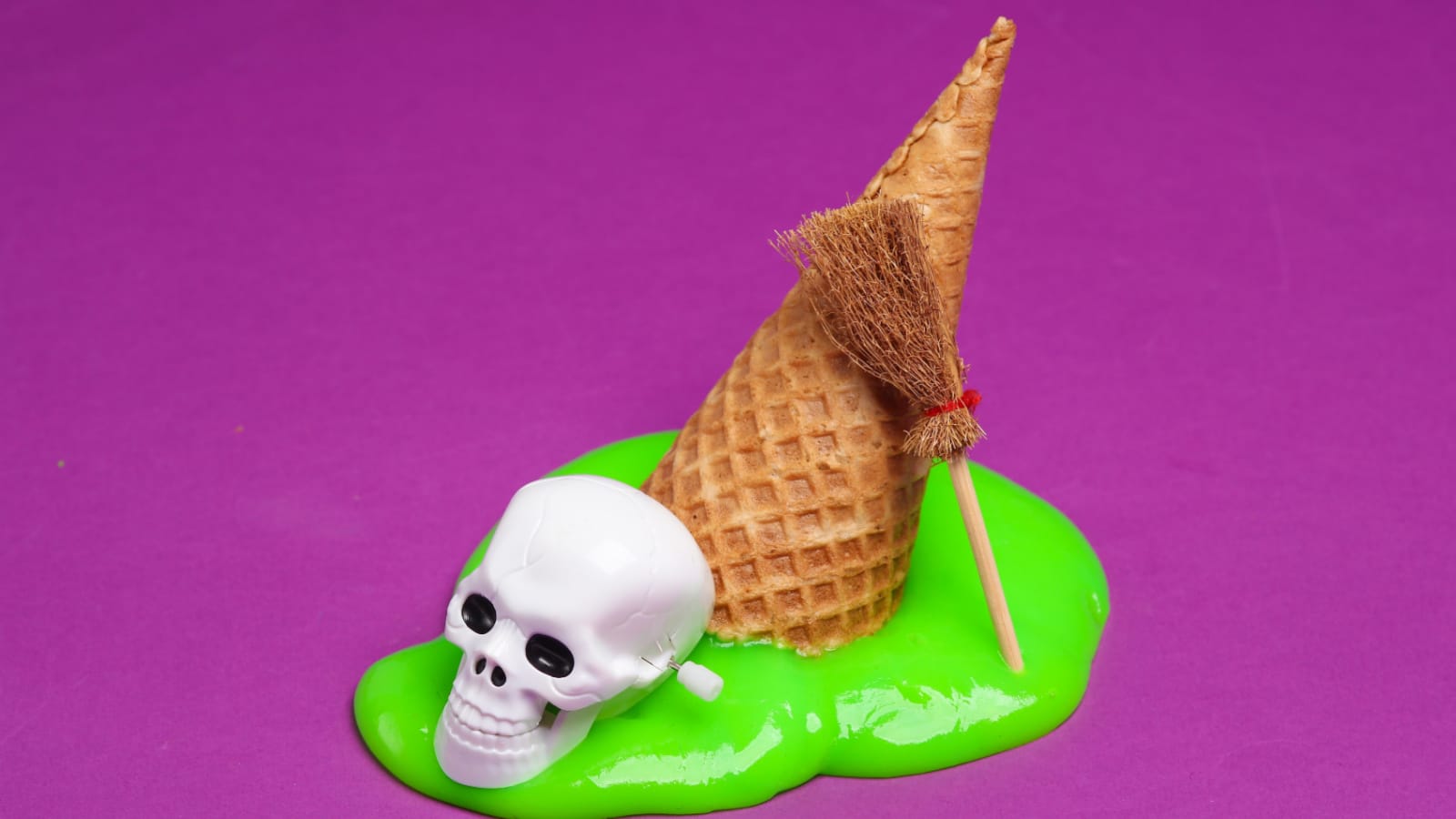 Waffle cone with green slime, skull and witch's broom on a purple background. Minimal halloween layout