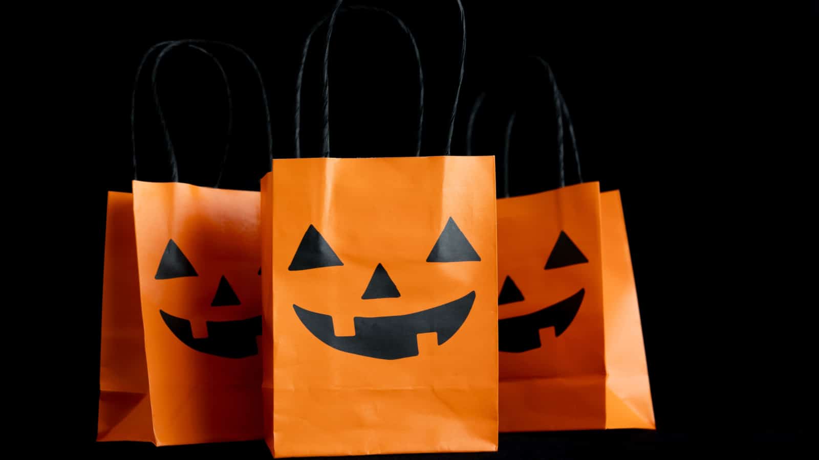 Halloween treat bags for trick-or-treating sweets candies. Paper gift bags with handles, for candy and other goodies. Decorated with spooky Jack-o'-lantern face. Trick or Treat party favor bags.