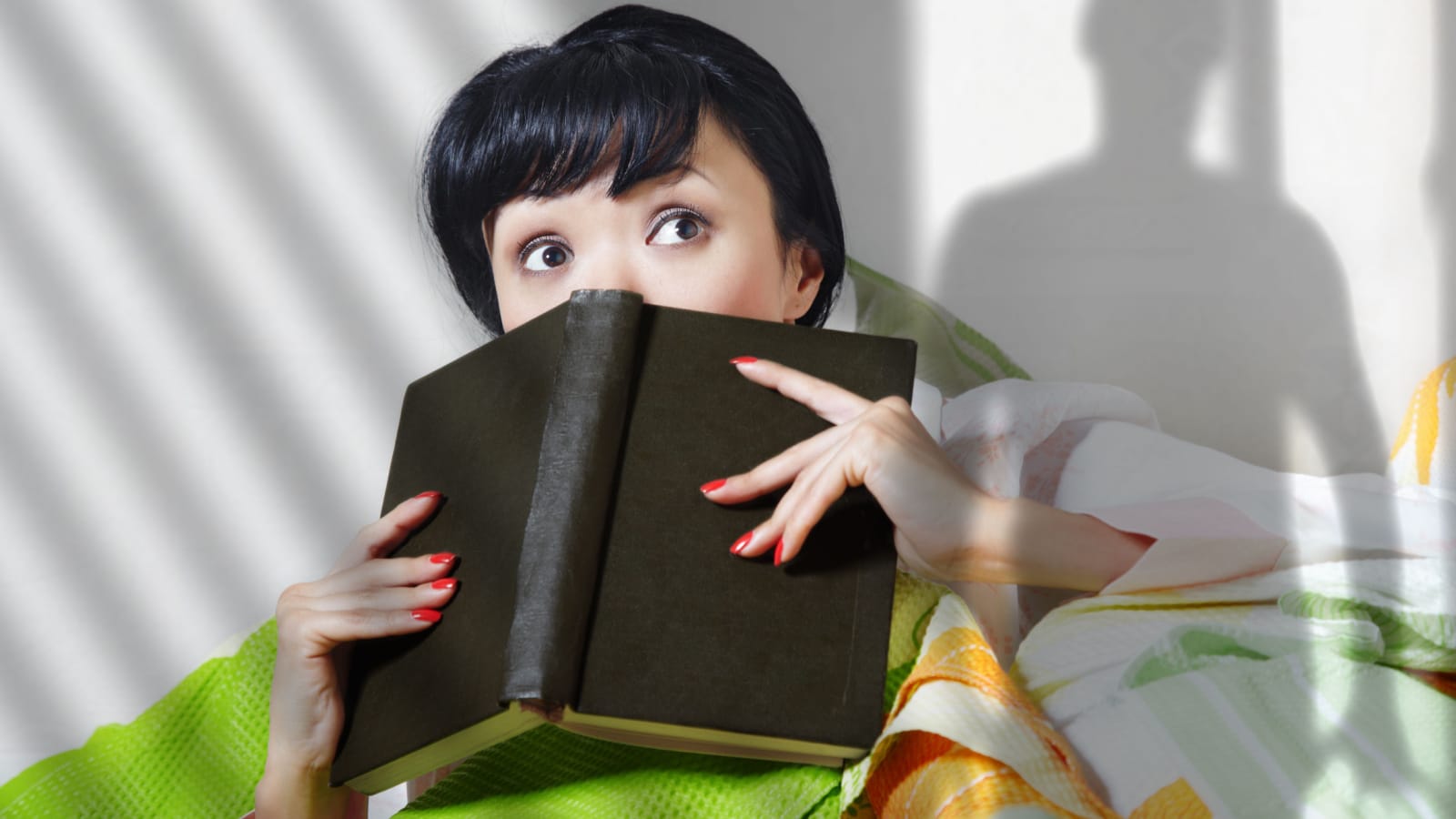 Afraid lady with book indoors looking to somebody. Shadow of somebody is on the wall