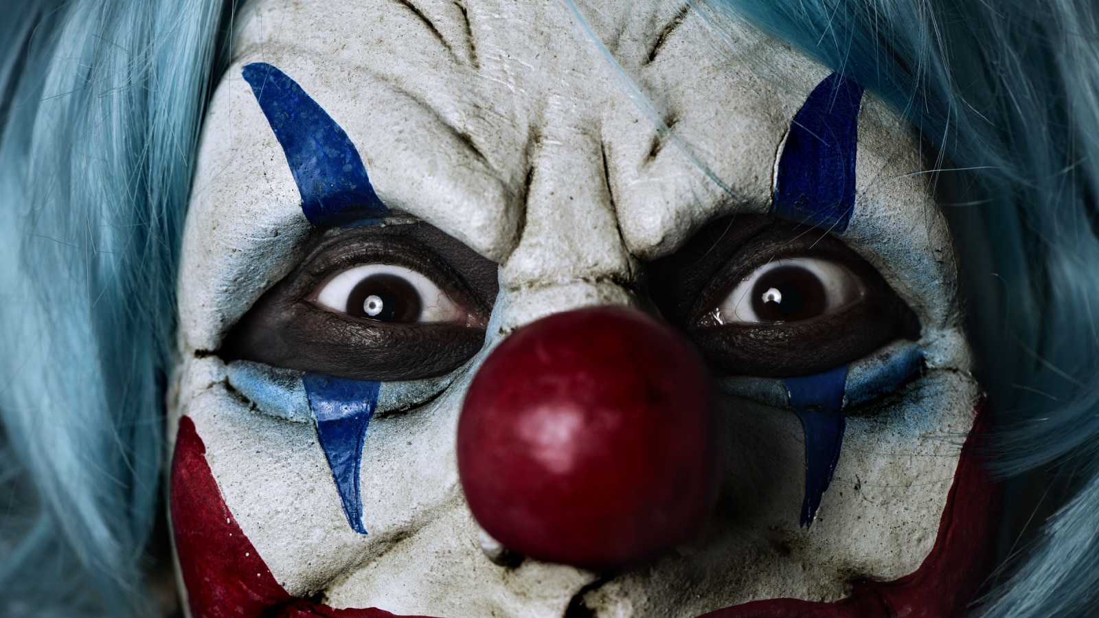closeup of a scary evil clown wearing a blue hair wig