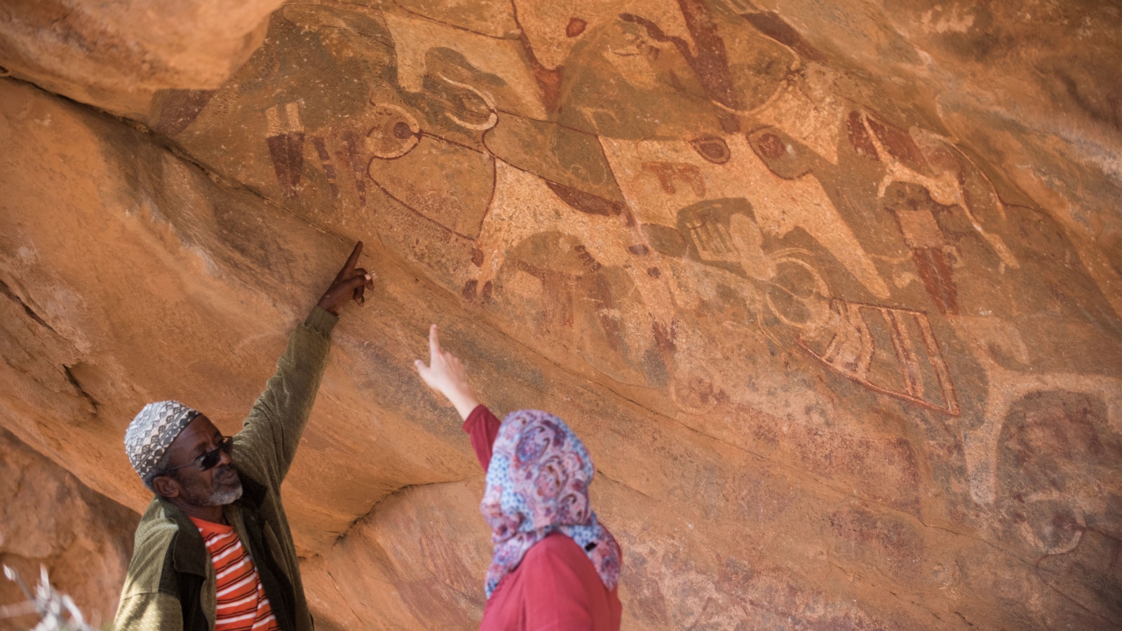 HARGEISA, SOMALILAND - 13 JANUARY 2016: a guide shows a tourist to her amazement the place in a cave wall of Las Geel where giraffes are depicted. Nowadays giraffes do not longer inhabit this area.
