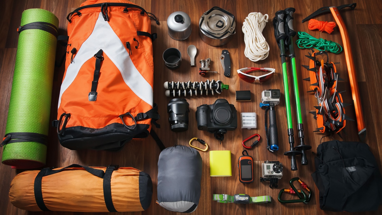 Equipment for mountaineering and hiking on wooden background. Climbing equipment: rope, trekking shoes, crampons, ice tools, ice ax, ice screws, red knife and other set on dark wooden background.