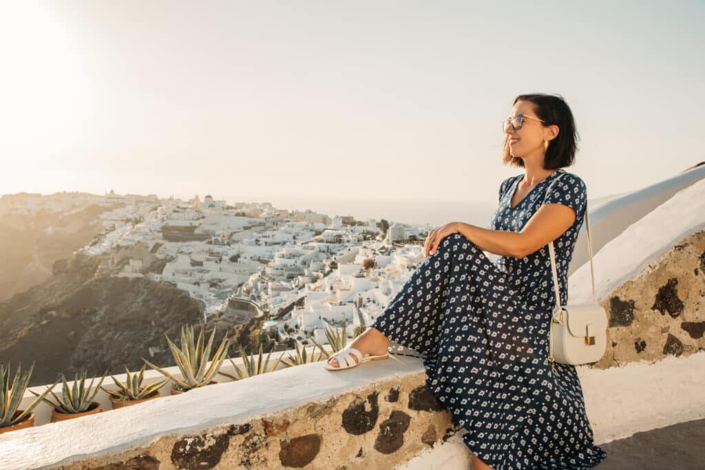 Lindsey of Have Clothes, Will Travel in Santorini Greece wearing white YSL tribute sandals and a navy Karina Dress