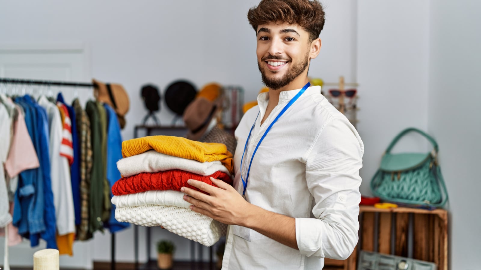 Young arab man shopkeeper holding folded clothes working at clothing store